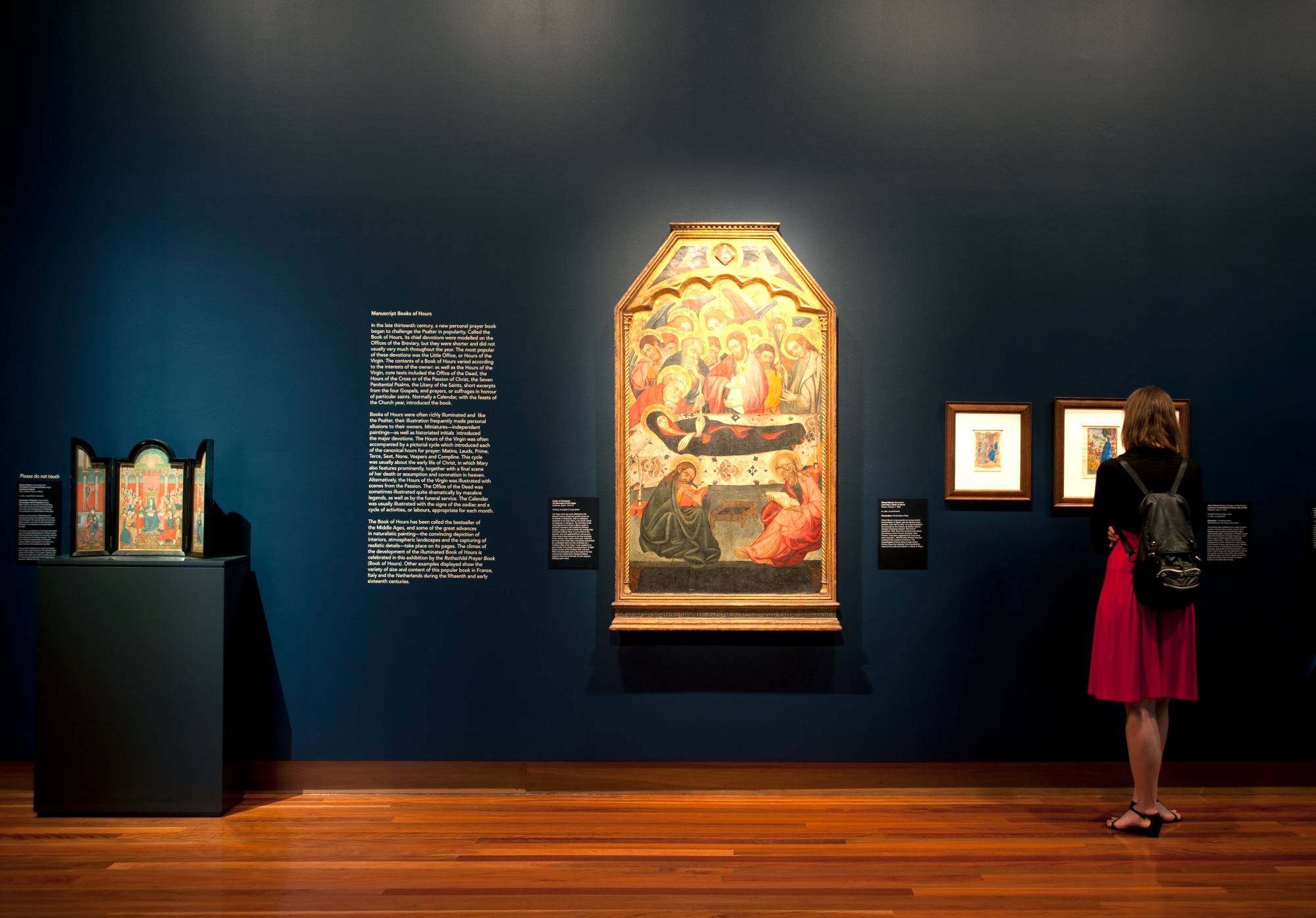 A dark gallery with  large medieval painting on a black-painted wall surrounded by smaller works