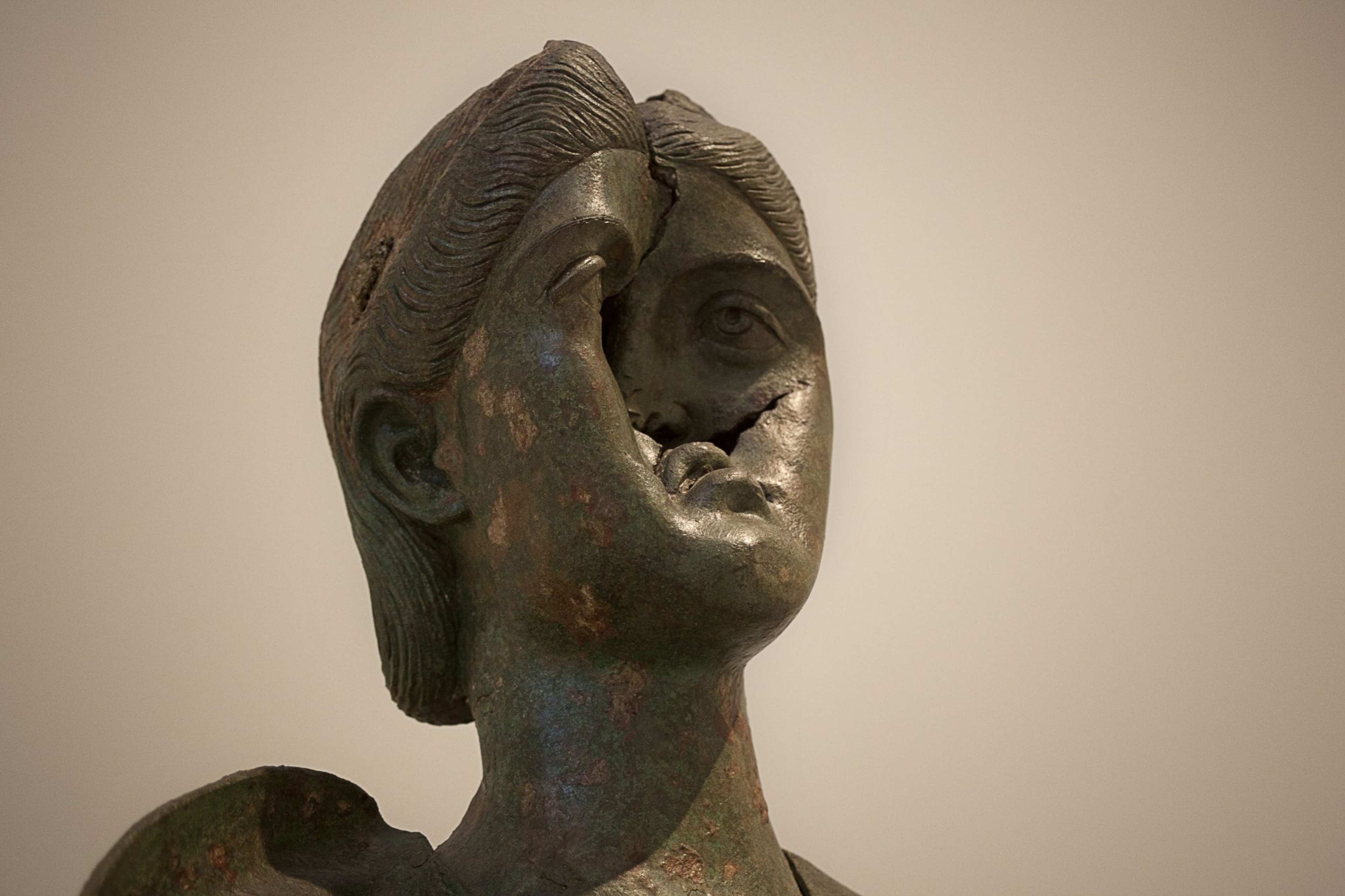 A photograph of a sculptural head cast from metal with the face smashed in