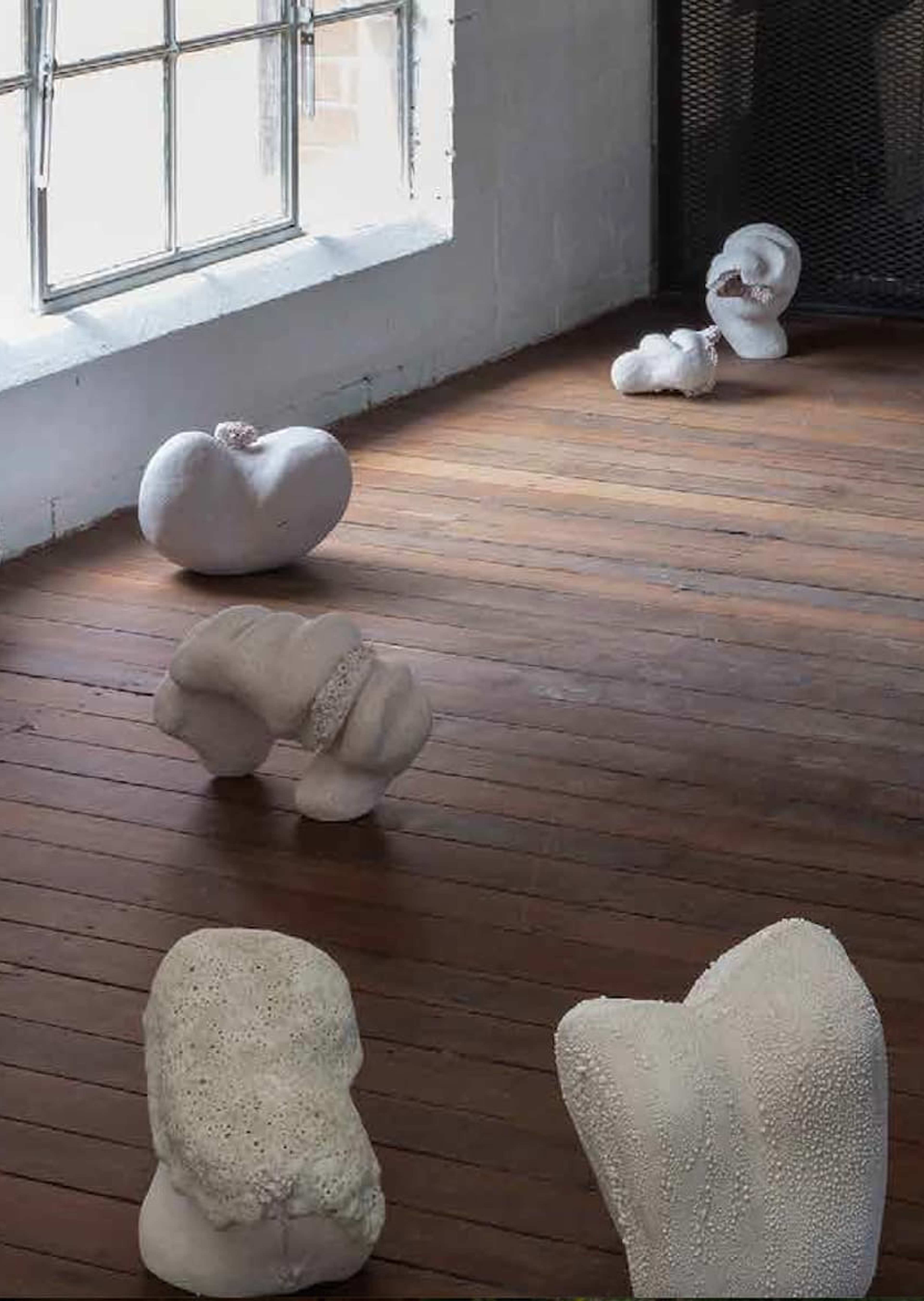 White abstract sculptures are scattered across a wooden floor near a large window, with the word “UNPREDICT” in bold yellow text on the right side of the image.