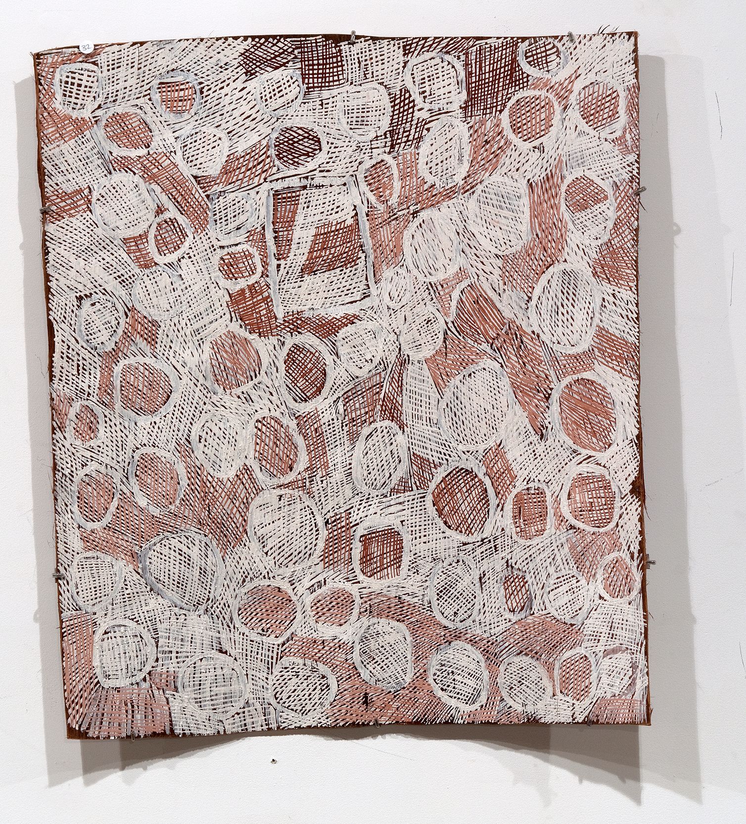 A bark paintings with cross-hatched ovals filling warm brown cross-hatched background, one square shape hiding between the ovals.