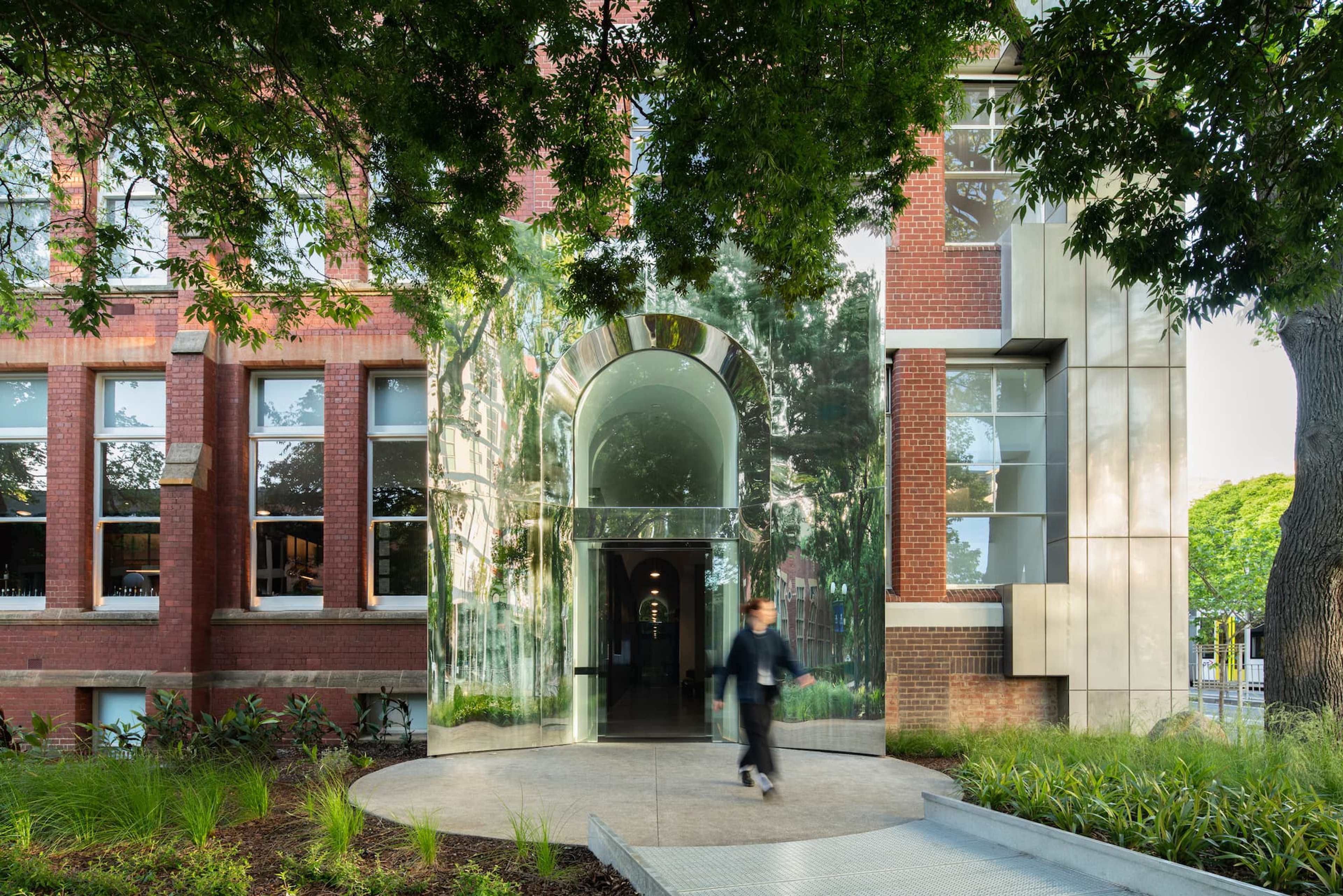 A person walking in front of a brown brick building with silver metalic entranceway.
