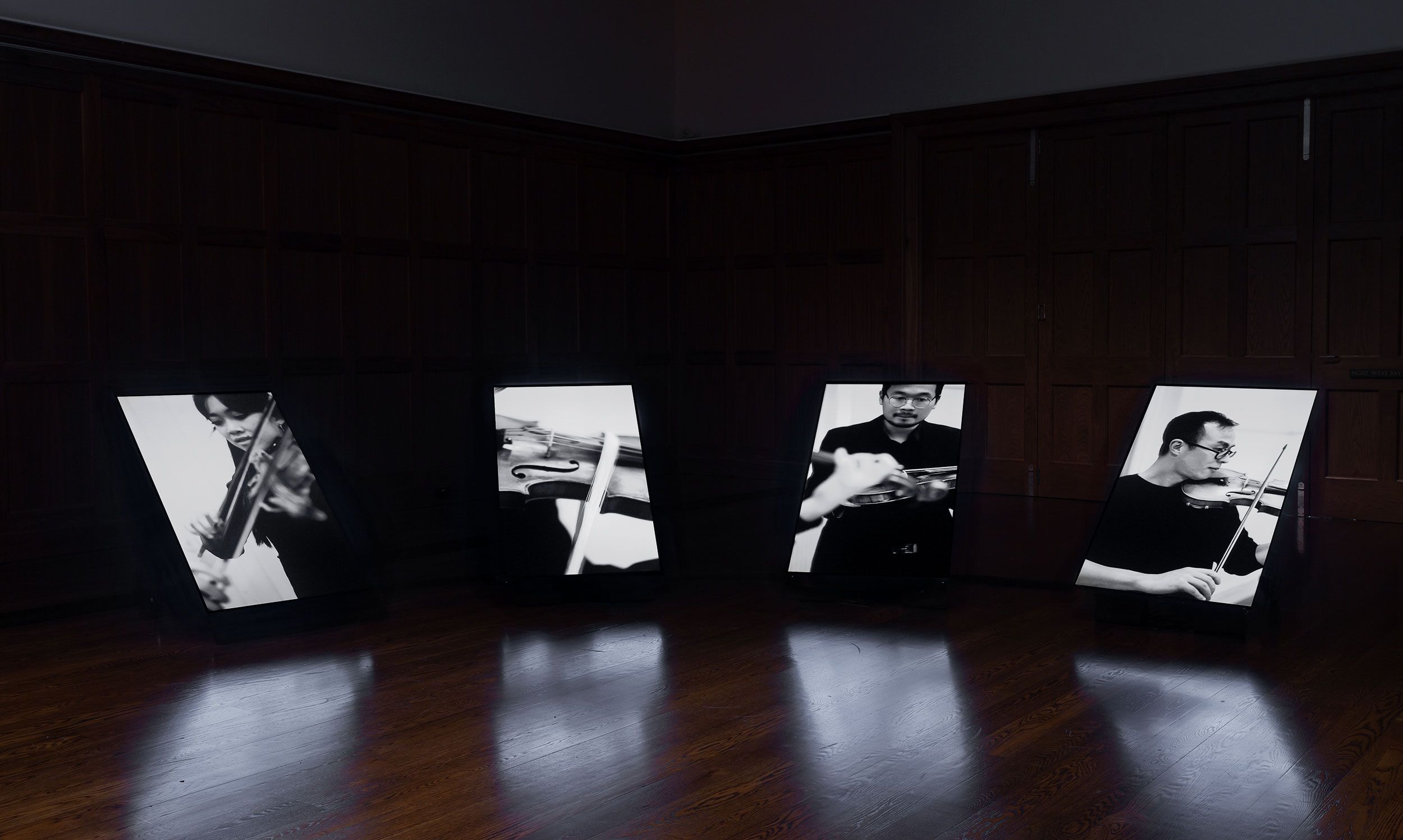 Four portrait screens showing musicians playing violin in black and white