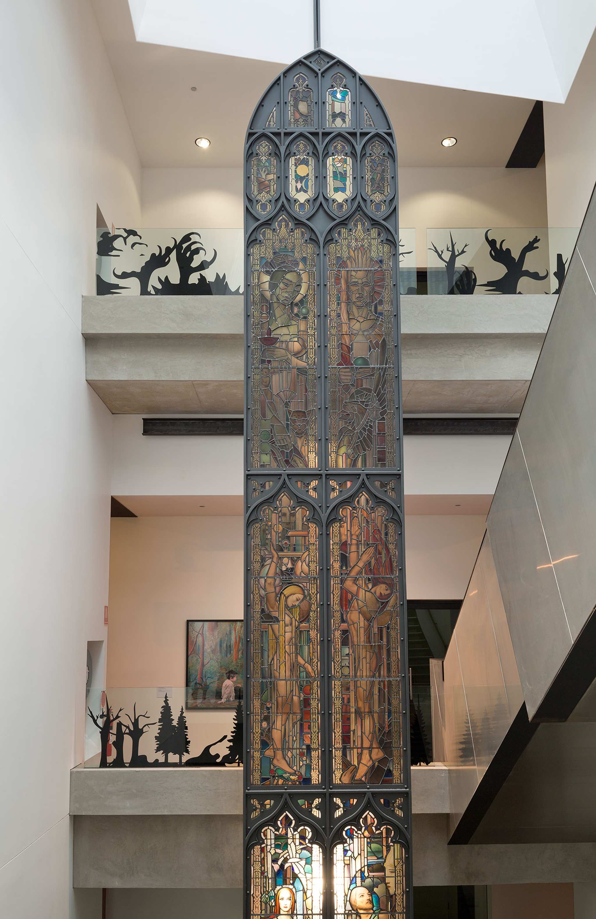 A photograph of a building's foyer spanning several levels with stained glass window column in the centre