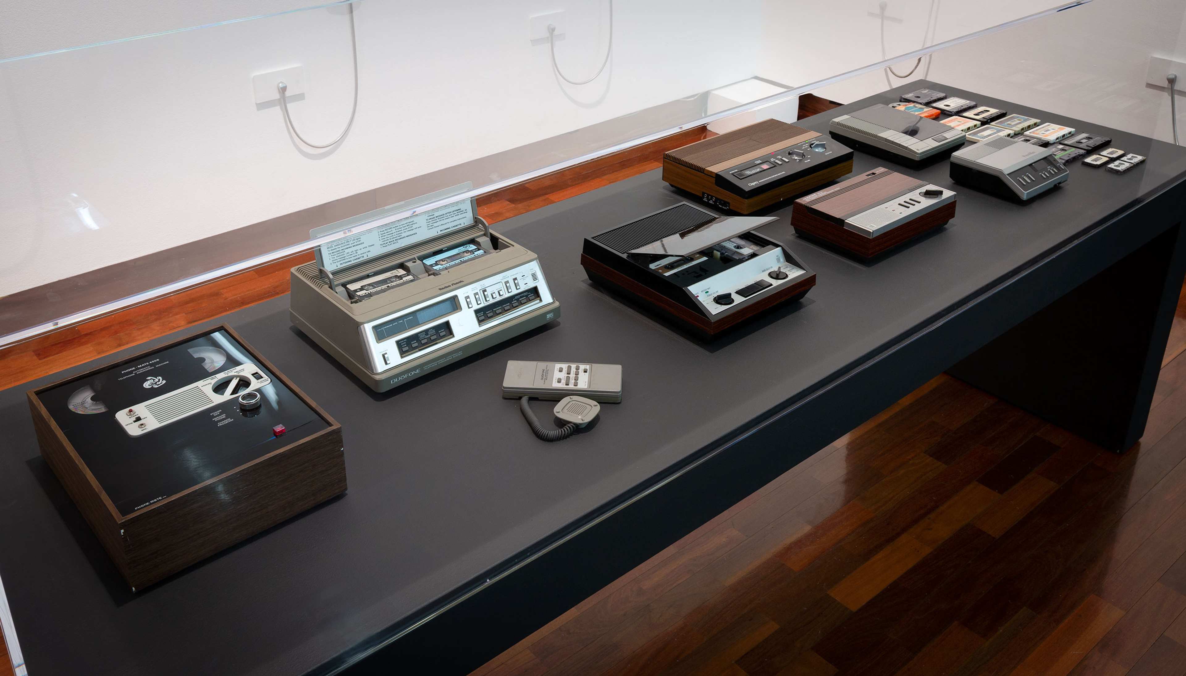 A collection of vintage answering machines and voice recorders in a vitrine