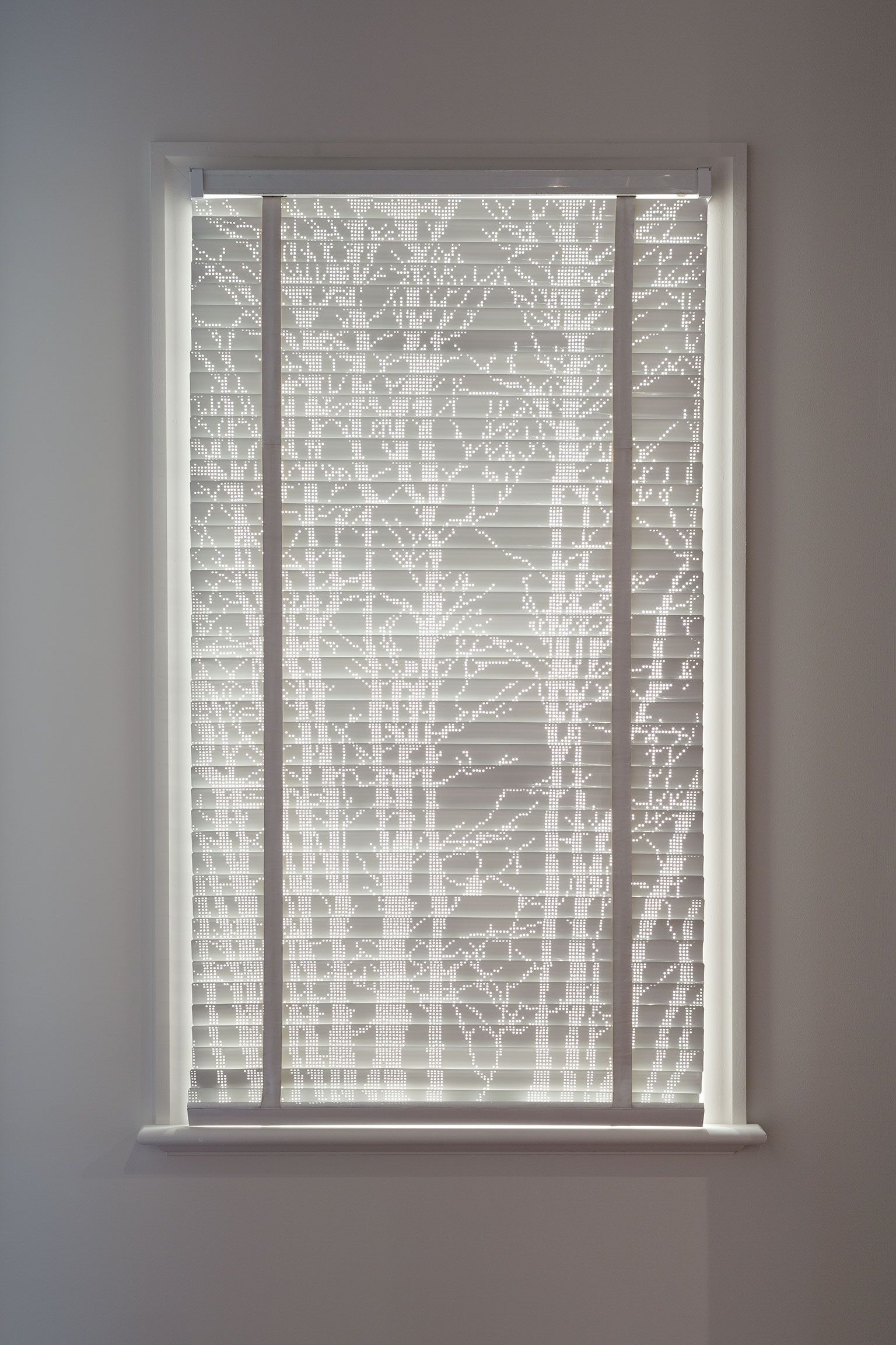 A photograph of a venetian blind with the light coming through the perforations in the slats forming the silhouettes of trees