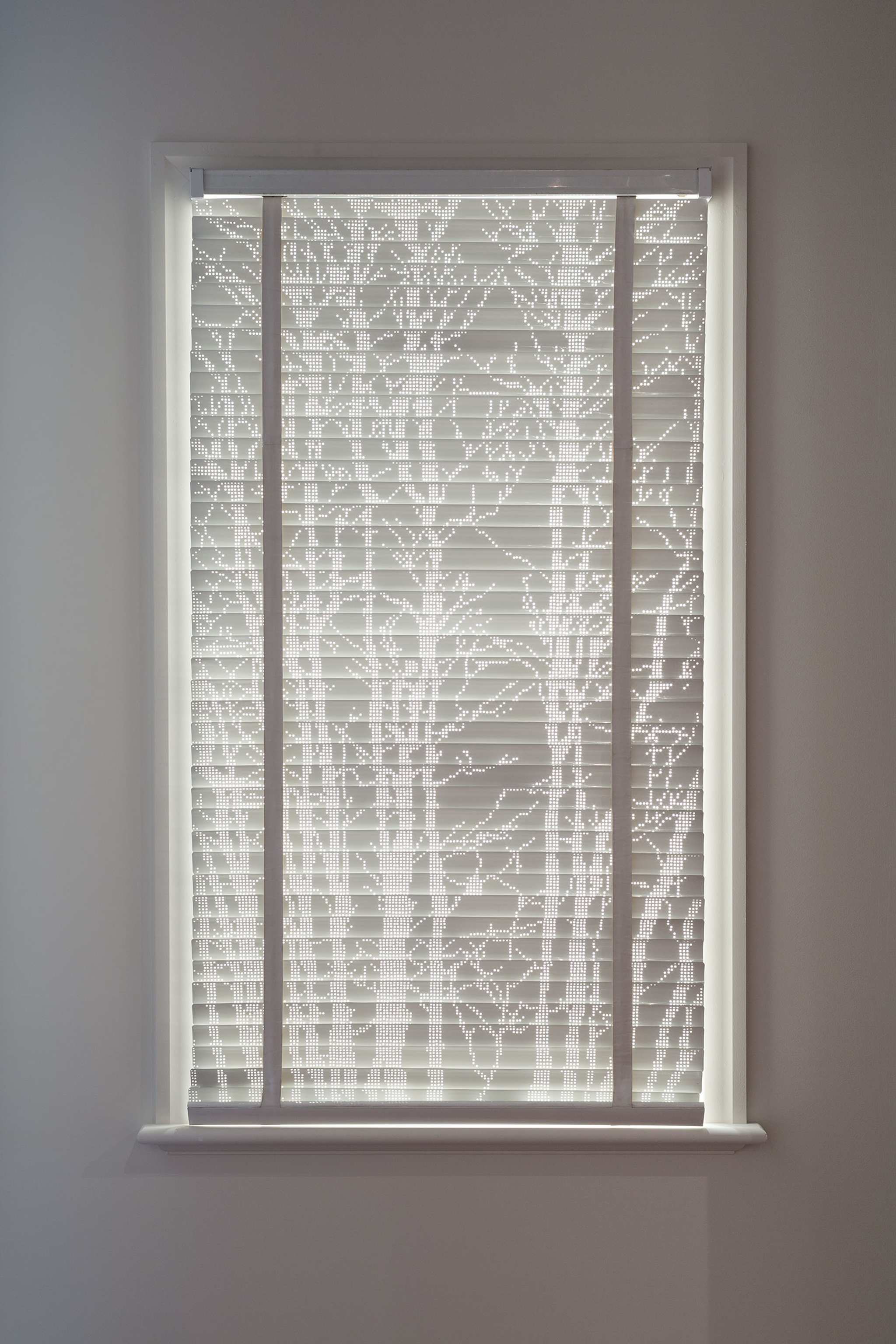 A photograph of a venetian blind with the light coming through the perforations in the slats forming the silhouettes of trees