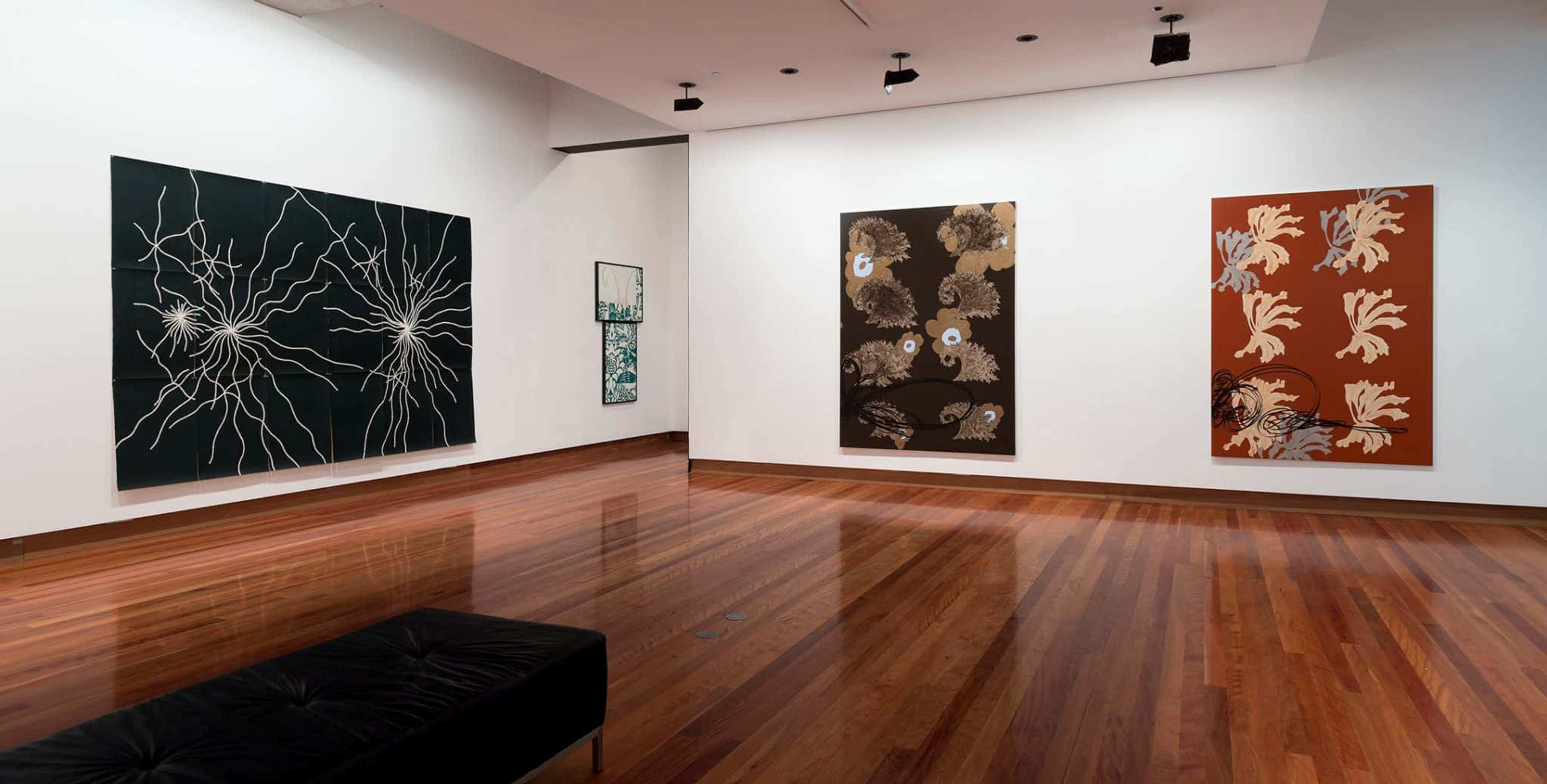 Three large abstract canvases in black, brown and red in the gallery space with white walls