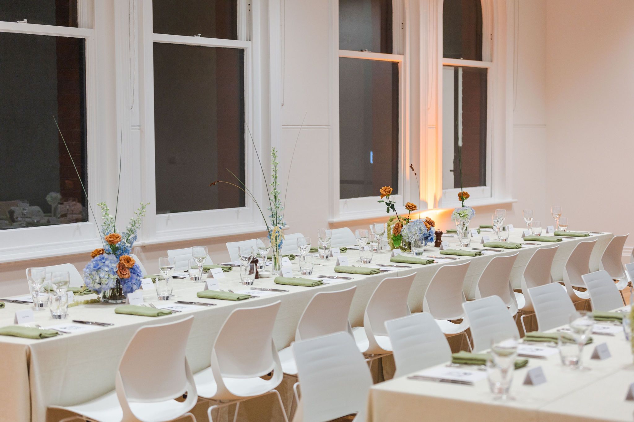 A formal dining setup with white chairs and tables decorated with blue flowers.