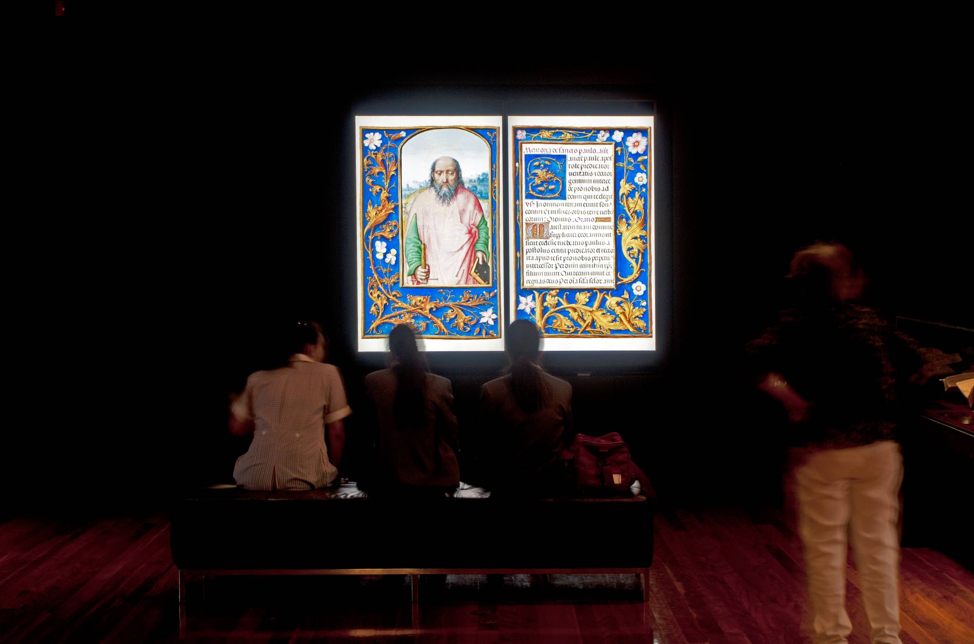 A group of people in a darkened gallery looking at a projection of enlarged illuminated manuscript