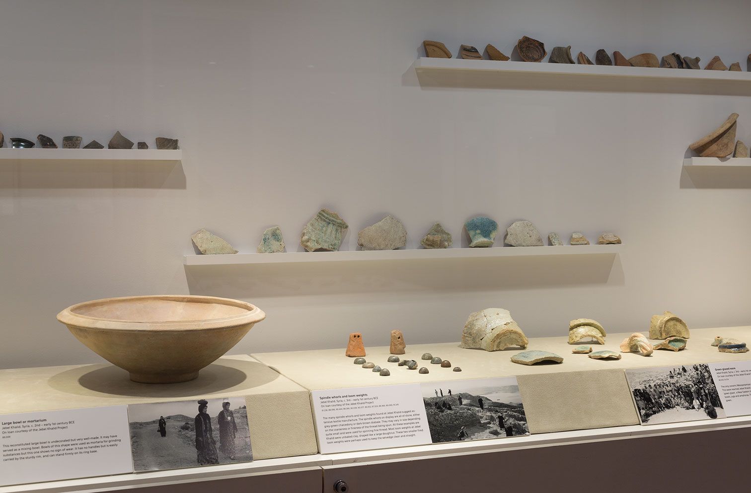 An image of a vitrine displaying an ancient ceramic vessel and various ceramic fragments arranged in rows
