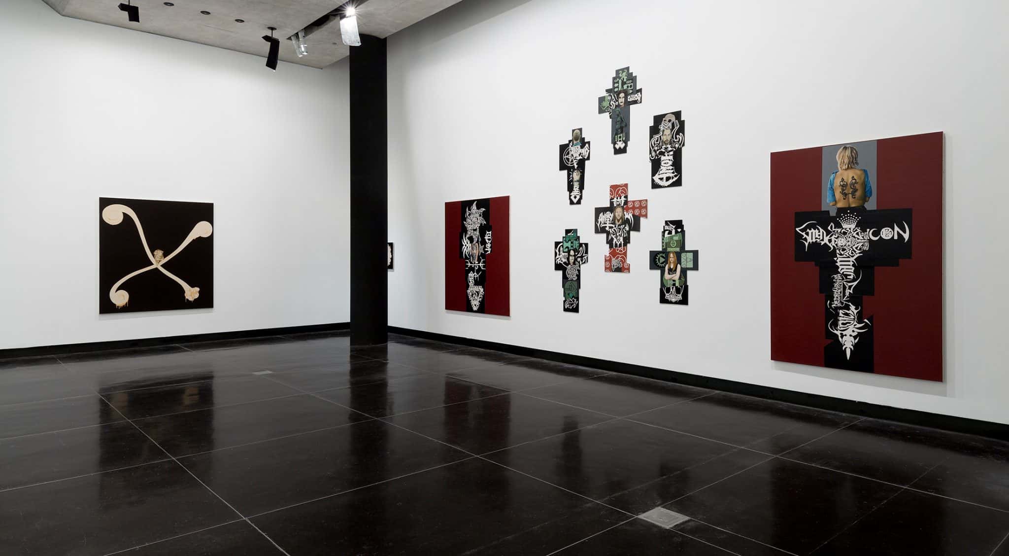 Three large abstract canvases in the shape of crosses or featuring motif of the cross in black, brown and red hang in the gallery space with white walls