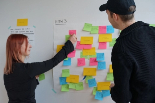 Two Humanoids employees standing in front of a wall with a poster and sticking post-its