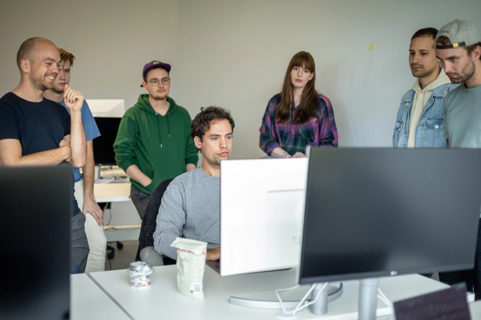 Iemand achter een computer met daaromheen een groep mensen dat meekijkt op hetzelfde beeldscherm.