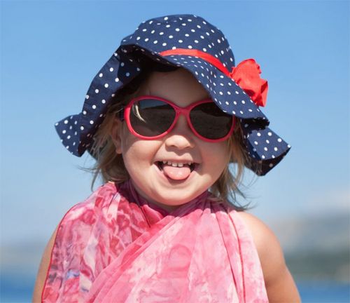 Bebe con lentes en la playa sacando la lengua.