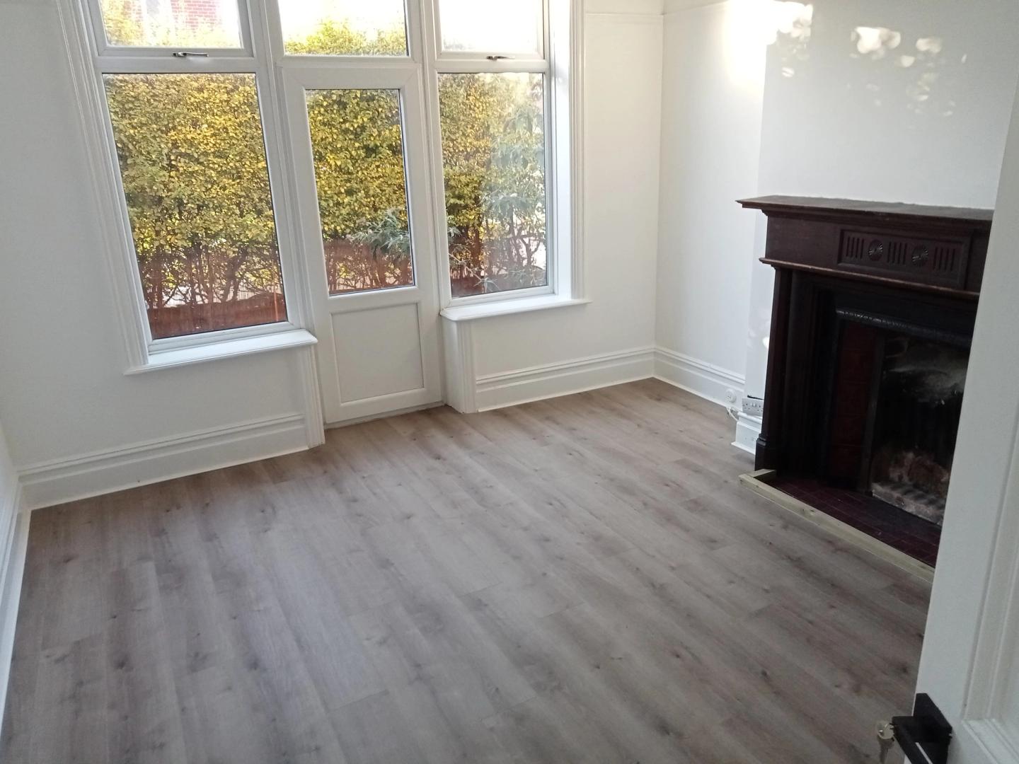 Freshly cleaned empty living room with a bay window, wood floor and fireplace