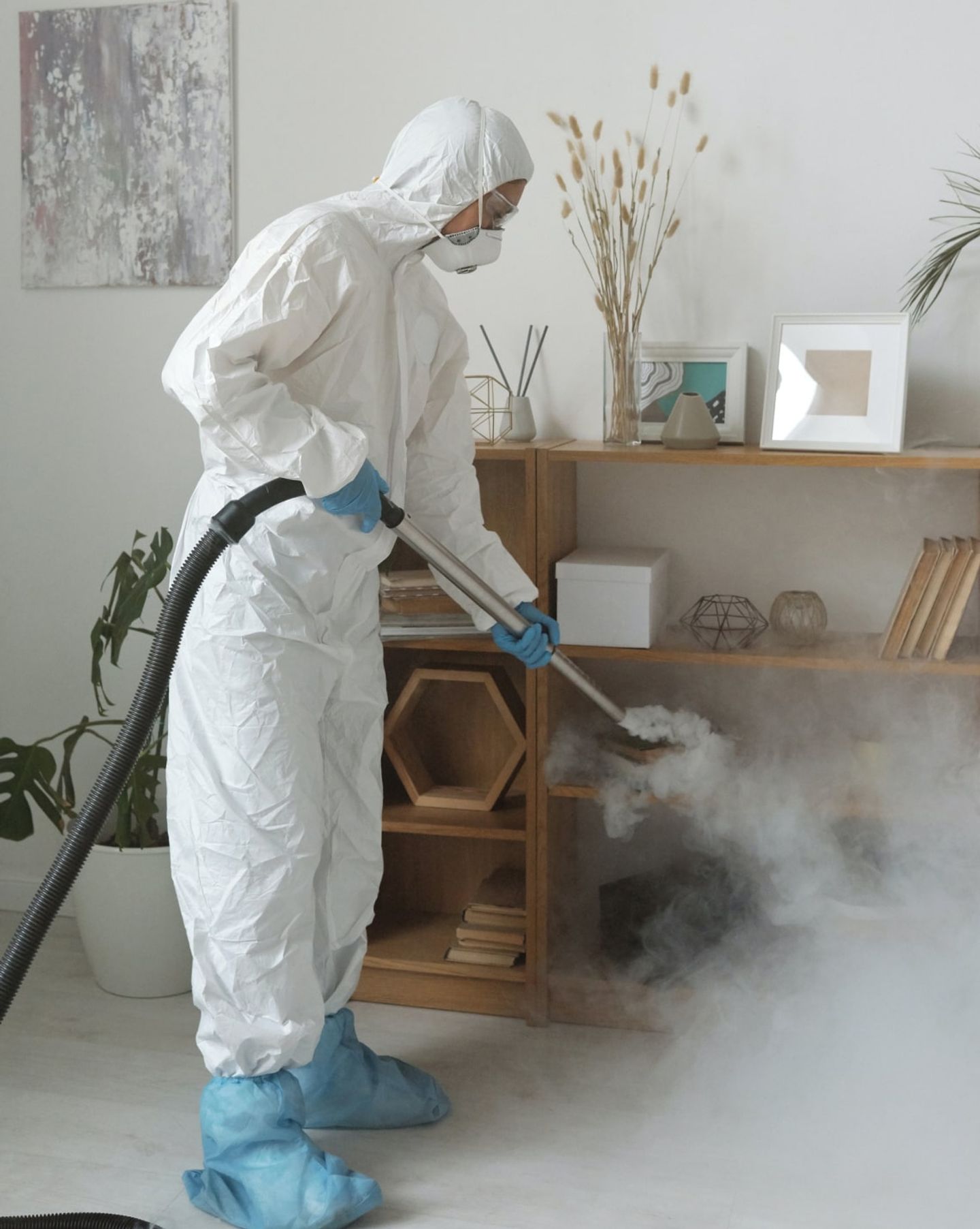 Cleaner in a protective suit and mask steam-disinfecting a wooden shelving unit