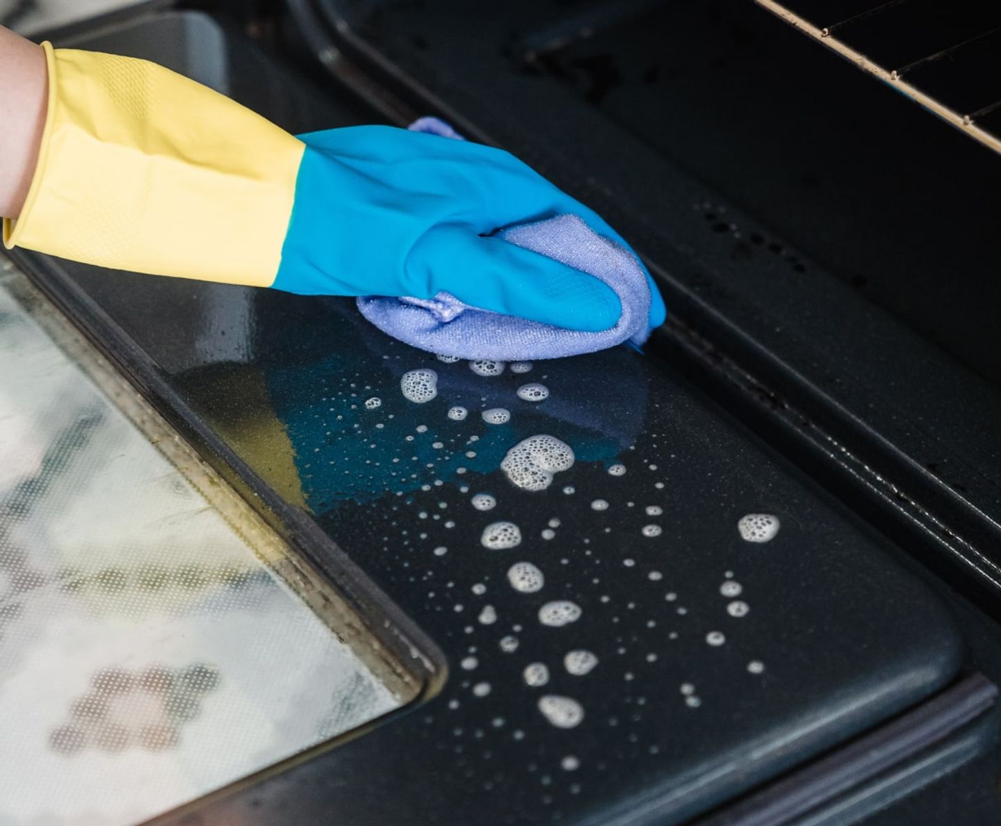 Cleaner wiping the soapy inside of an oven door with a cloth
