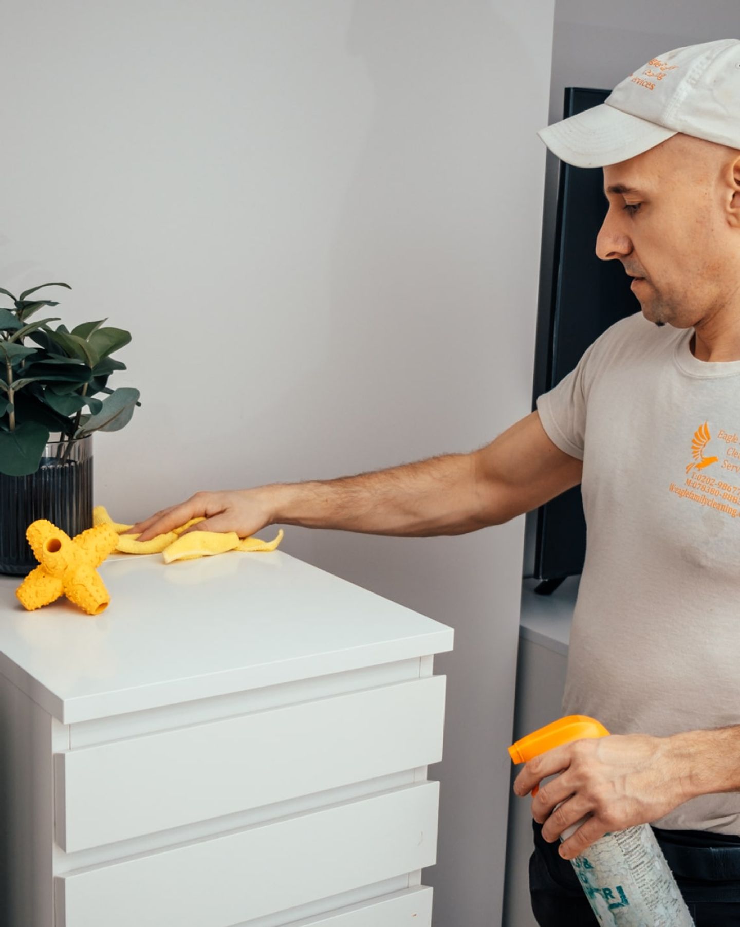 Eagle Family cleaner in branded uniform dusting a white chest of drawers