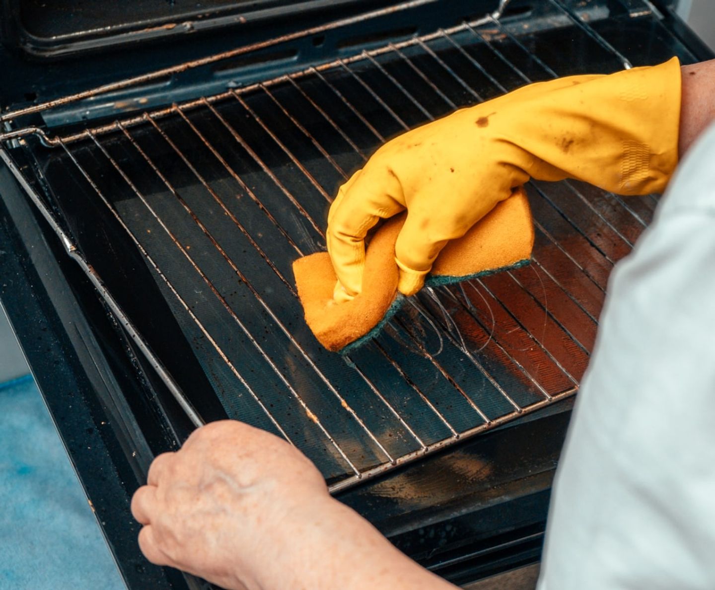 Cleaner in yellow gloves scrubbing an oven shelf rack with a sponge