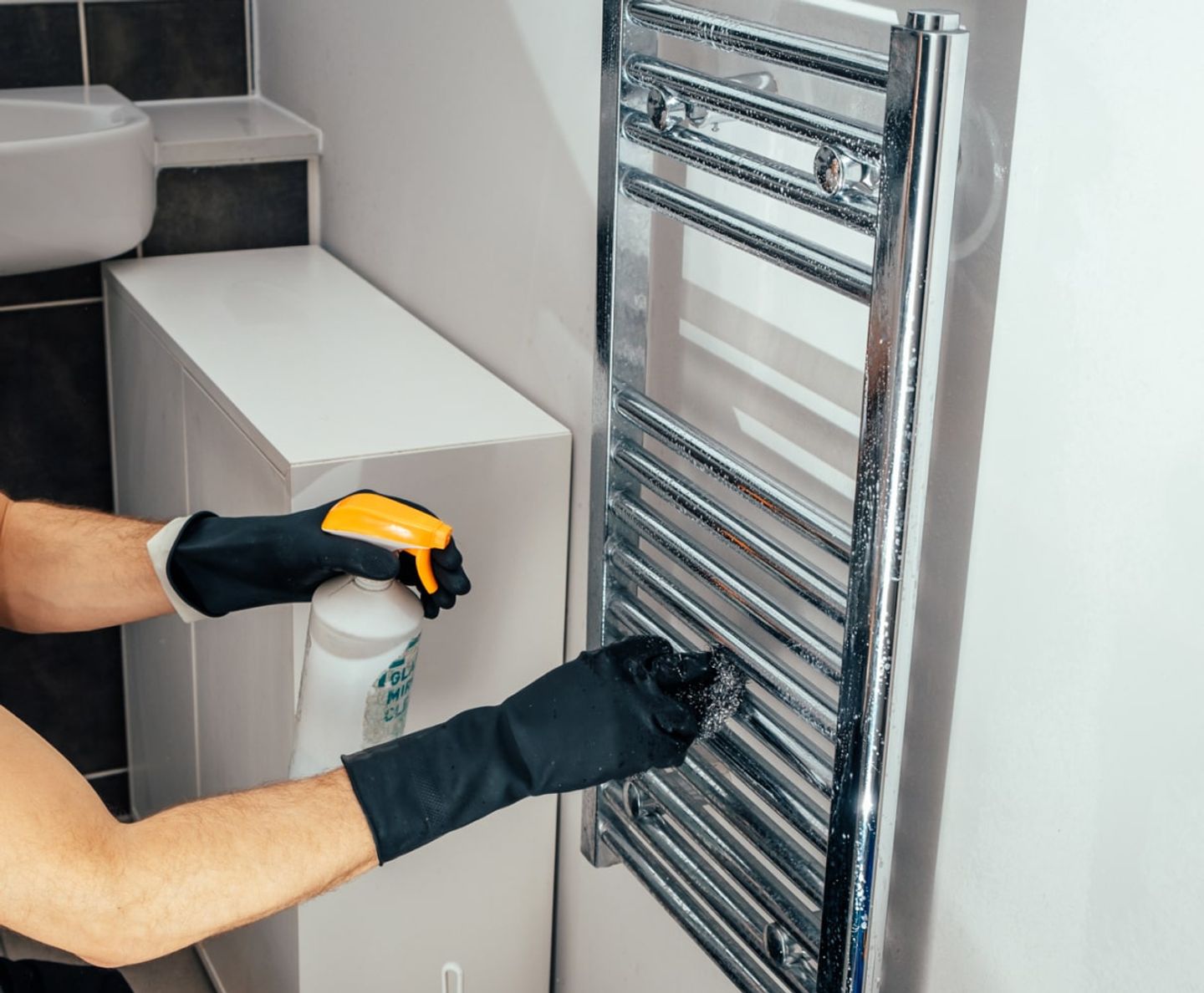 Cleaner polishing a chrome heated towel rail in a bathroom