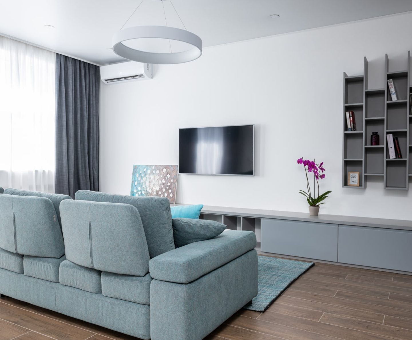 Clean modern living room with a teal sofa and wall-mounted TV