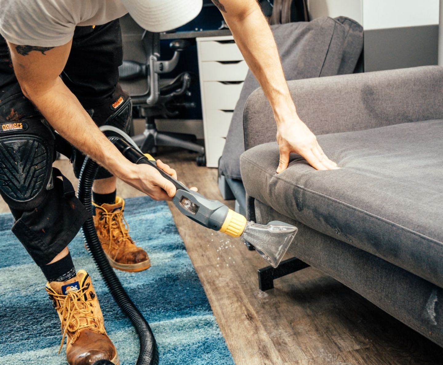 Cleaner deep-cleaning a grey sofa with an upholstery extraction tool