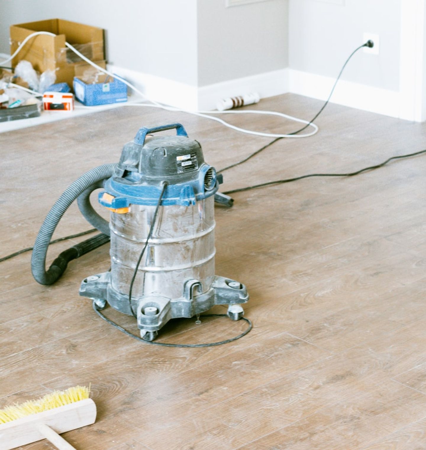 Wet-and-dry vacuum and stiff broom on a wood floor amid post-construction dust