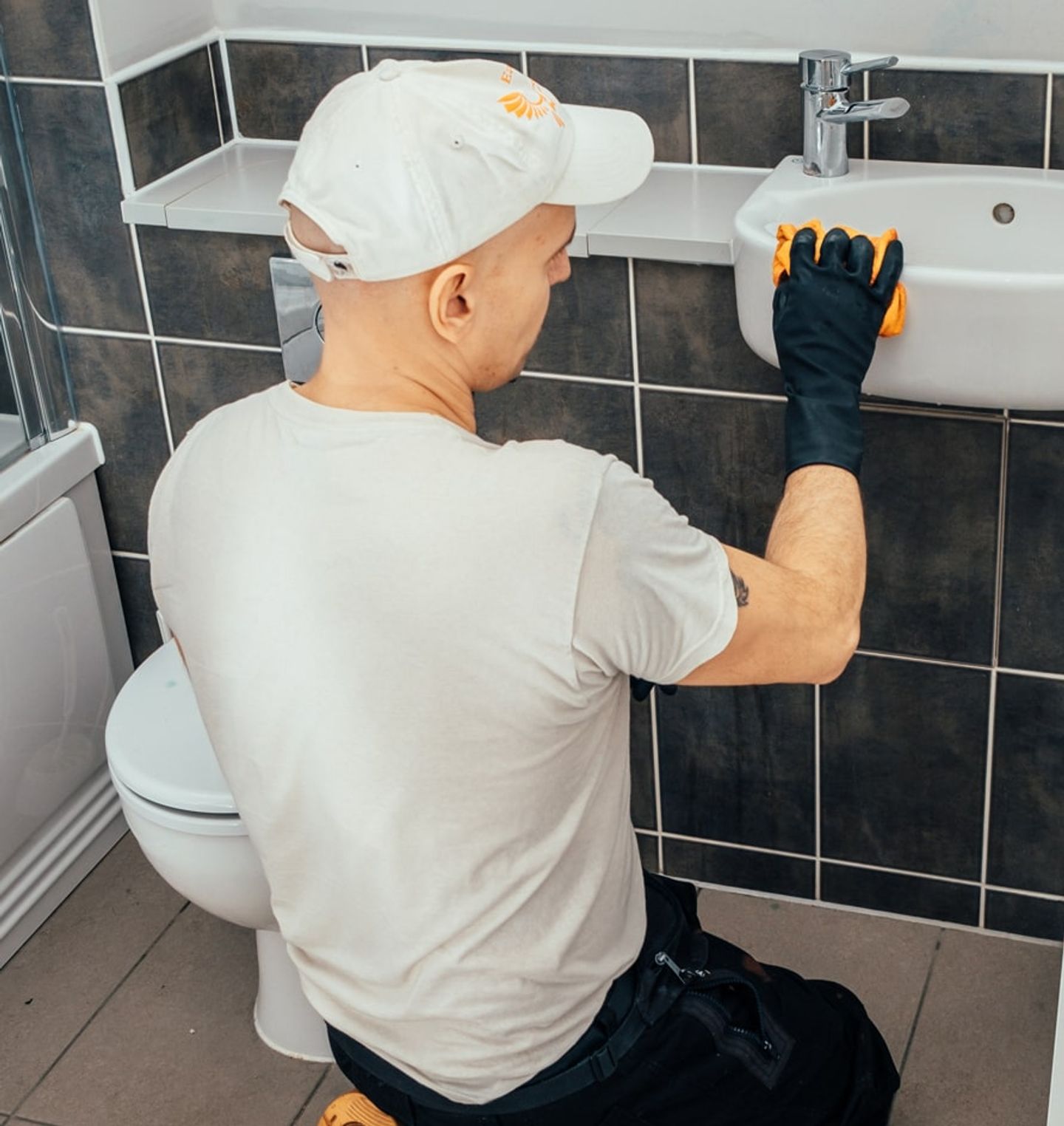 Eagle Family cleaner wiping a bathroom sink in a dark-tiled bathroom
