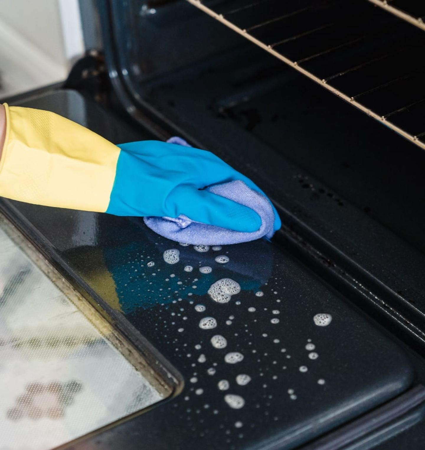 Gloved hand wiping down a soapy oven door