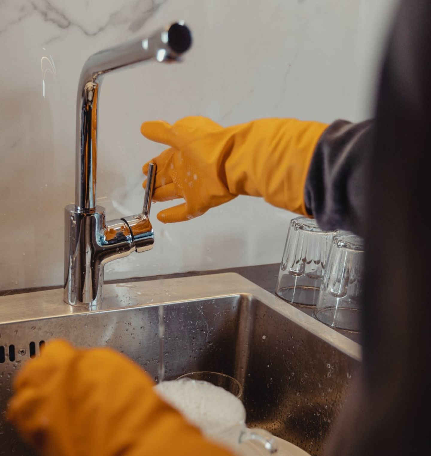 Gloved hands washing glassware at a kitchen sink