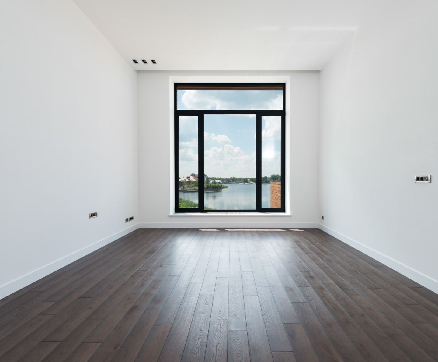 Empty room with a dark wood floor and large window overlooking a lake after building work