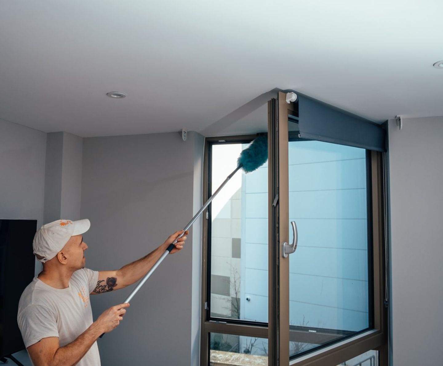 Cleaner dusting the top of a window frame with an extendable duster