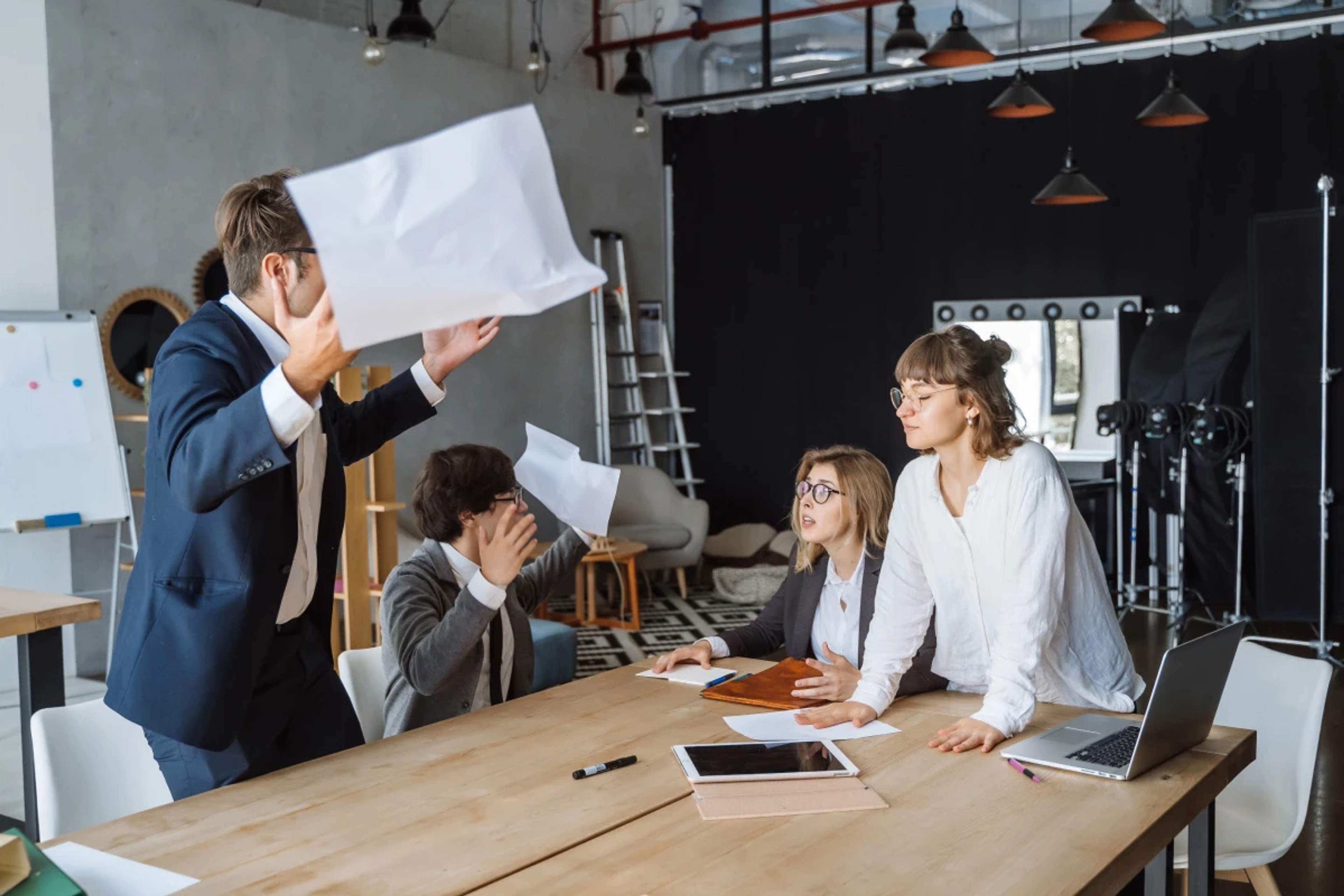 Creative team in a heated design discussion, one member standing while another throws papers in frustration.
