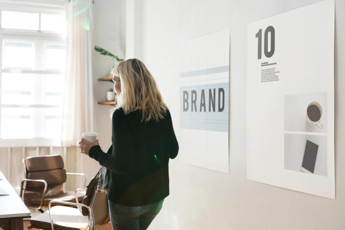 Woman holding a coffee cup in a modern office with brand posters displayed on the wall.
