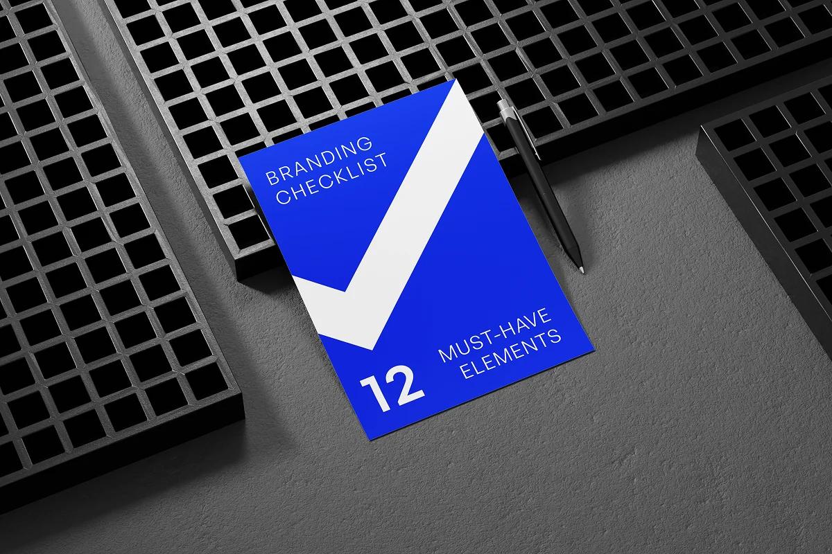 Blue branding checklist booklet titled “Branding Checklist – 12 Must-Have Elements” placed on a textured surface with a pen.