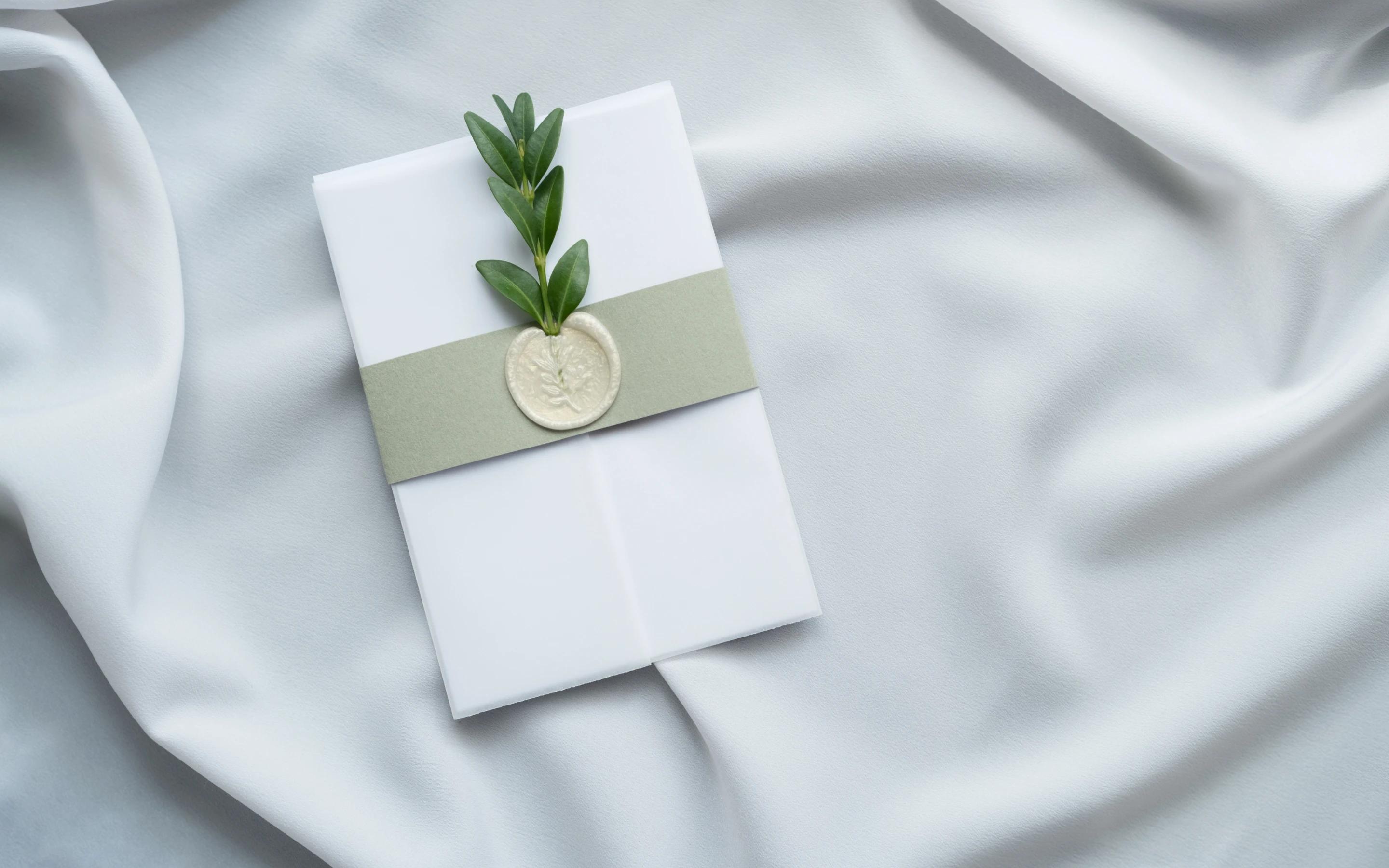 Elegant wedding invitation with botanical wax seal and olive branch on silk fabric background.