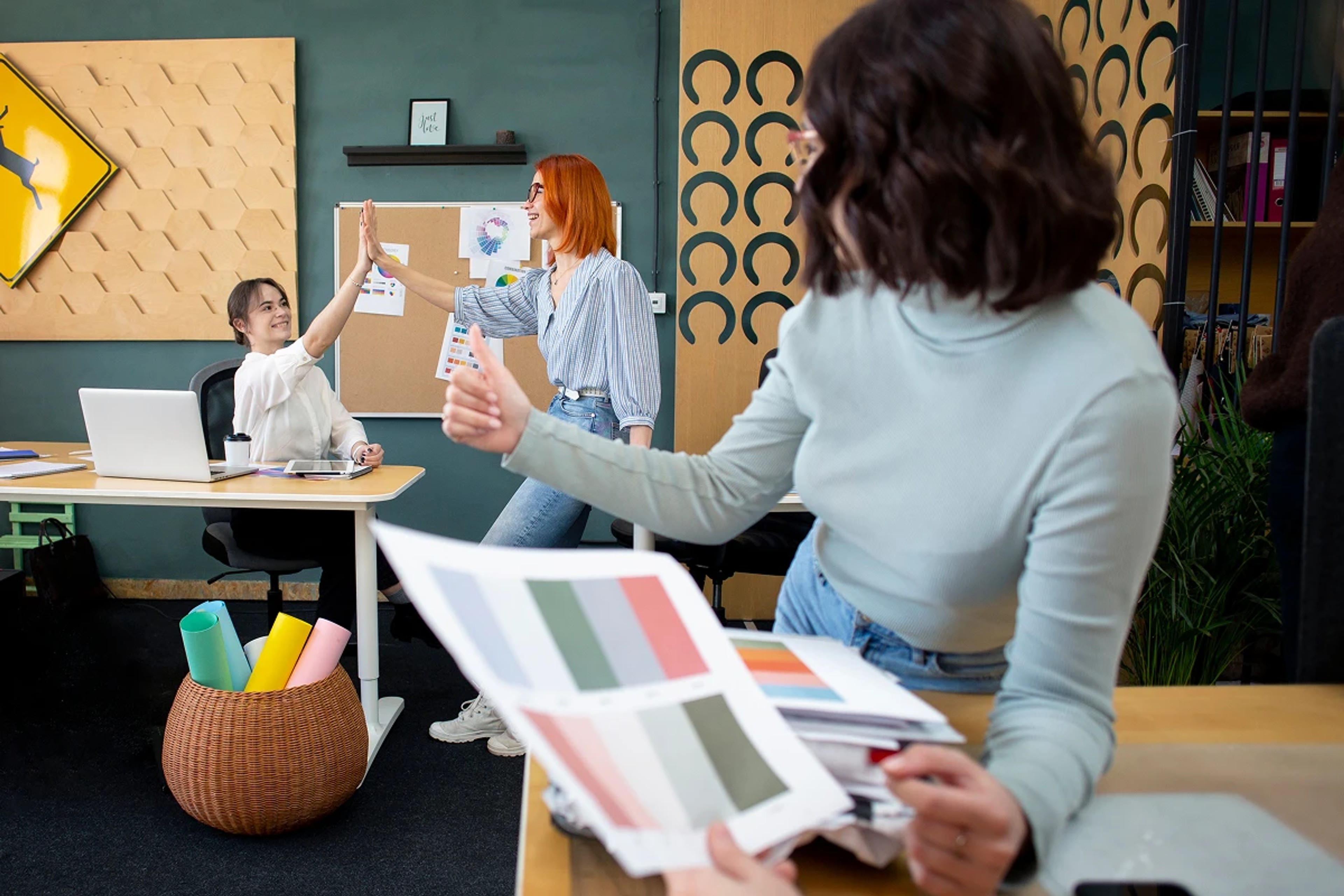 Creative team in a modern office exchanging high-fives and reviewing printed color palettes during a branding workshop.