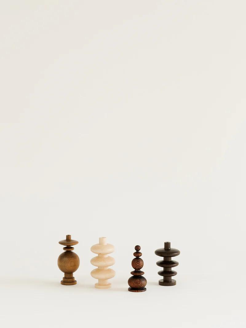 Four uniquely shaped wooden chess pieces in varying shades of wood stand in a row against a white background. Crafted in a woodturning studio, they feature smooth, rounded shapes and differ in height and design.