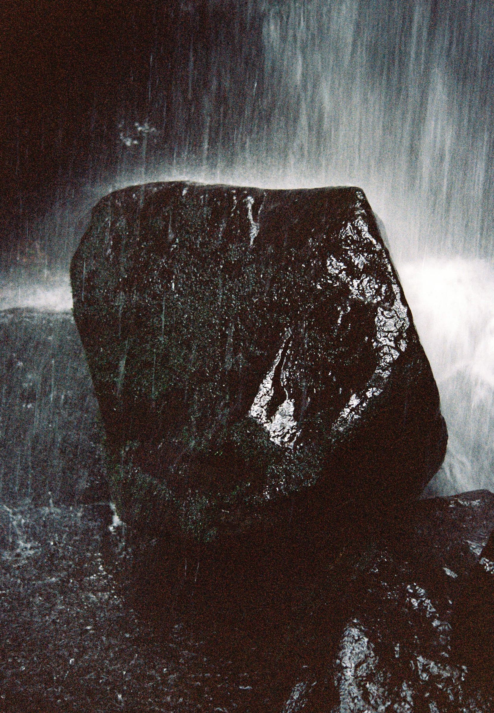 a wet rock sits underneath an active waterfall