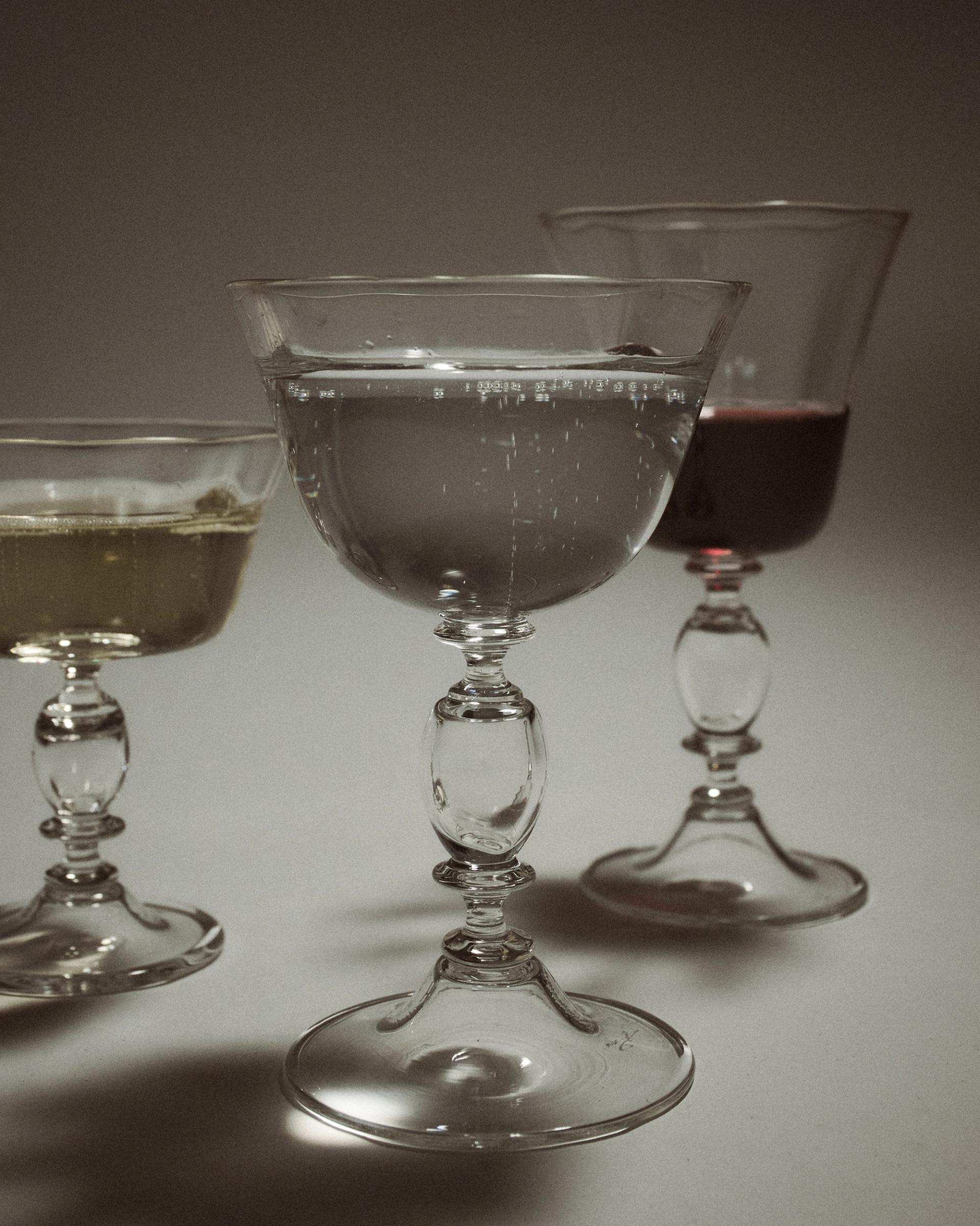 a collection of handmade glasses filled with wine and water in low light cast soft shadows