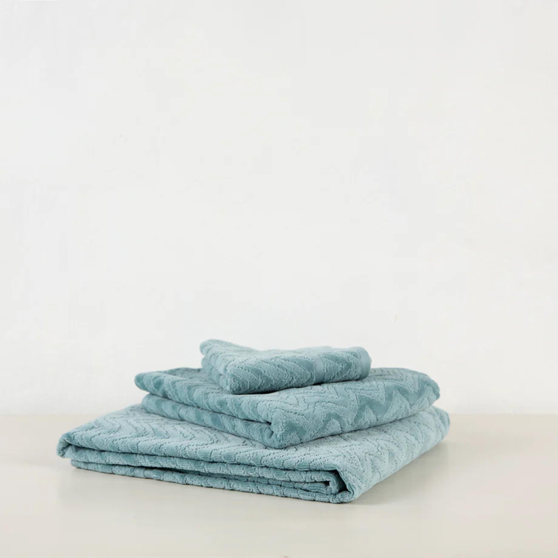 Folded light blue towels with subtle wavy pattern. Missoni-inspired texture on plain white surface against simple background.