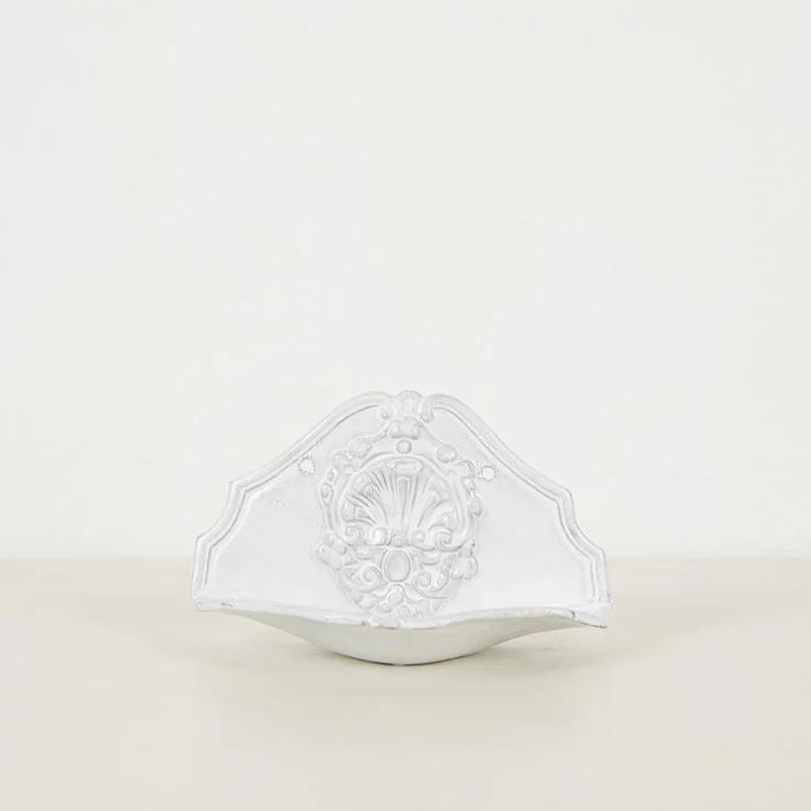 White ceramic wall fountain by Astier de Villatte. Ornate floral and leaf design with curved edge. Classical elegance against plain off-white background.