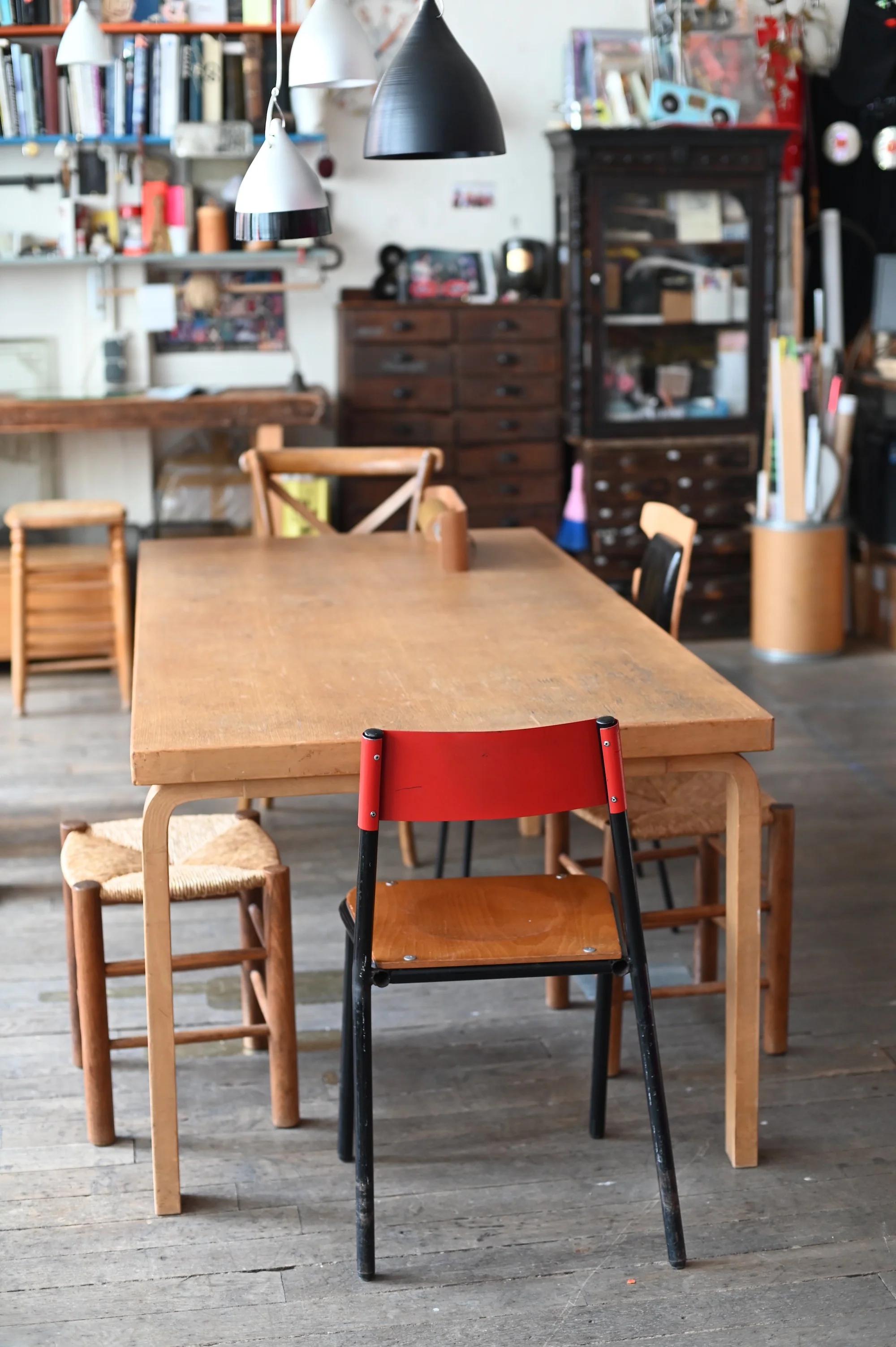 Dining area with wooden table and mixed chairs. Bookshelves, vintage cabinet, and pendant lights in background.