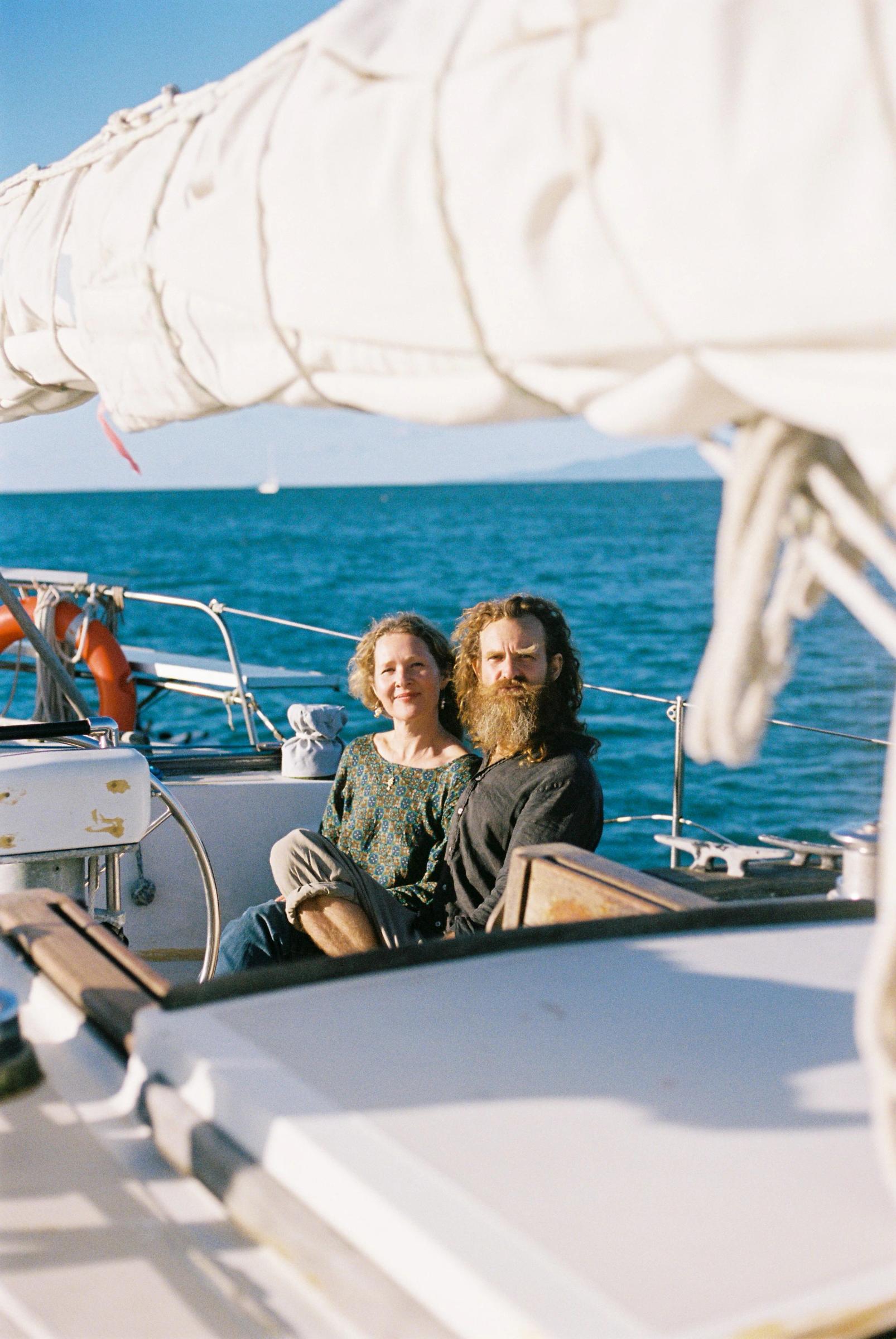 Man and woman on sailboat deck off Waiheke Island. Clear blue water and sky backdrop.