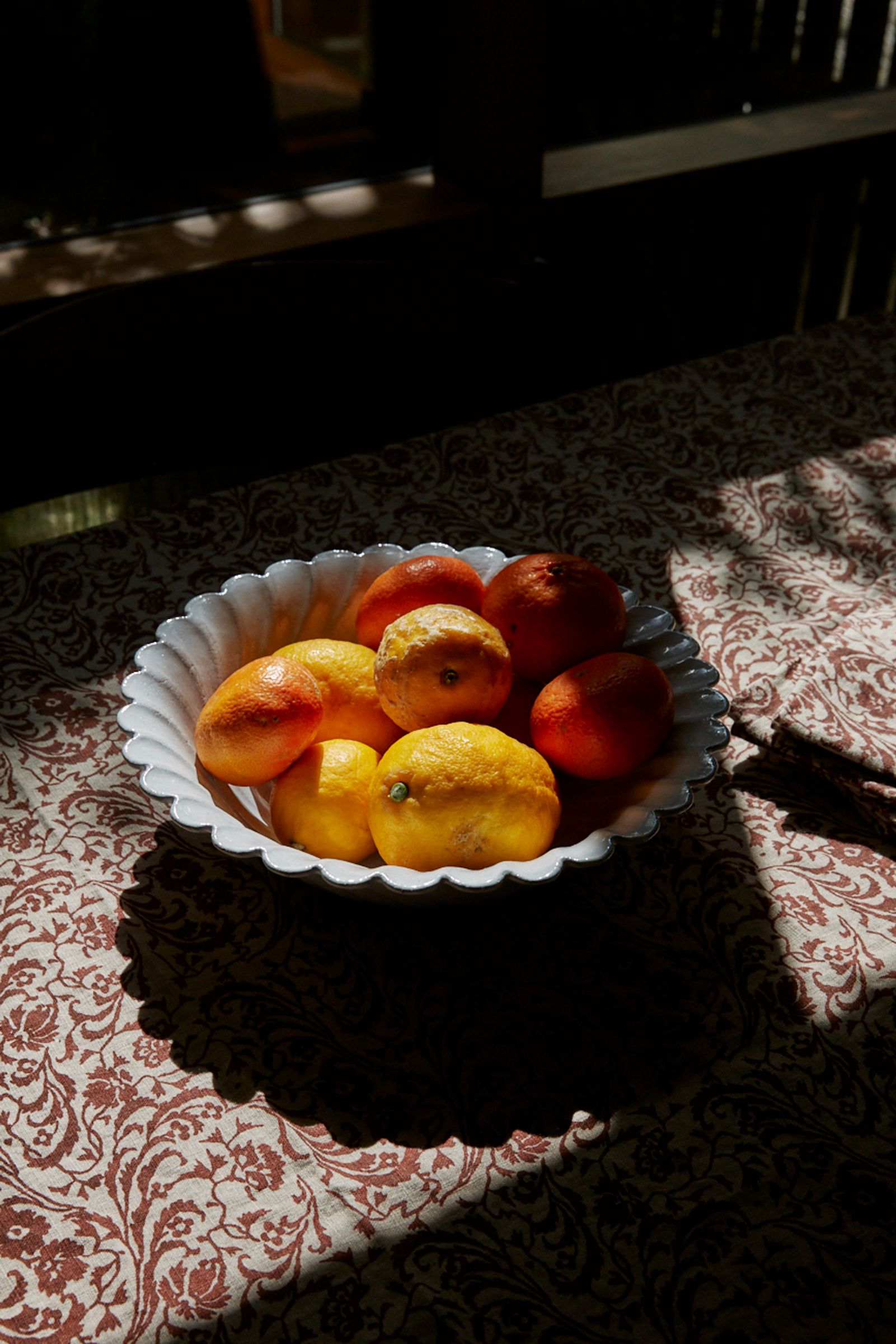 light falls over a cream and red tablecloth with a bowl of tomatoes