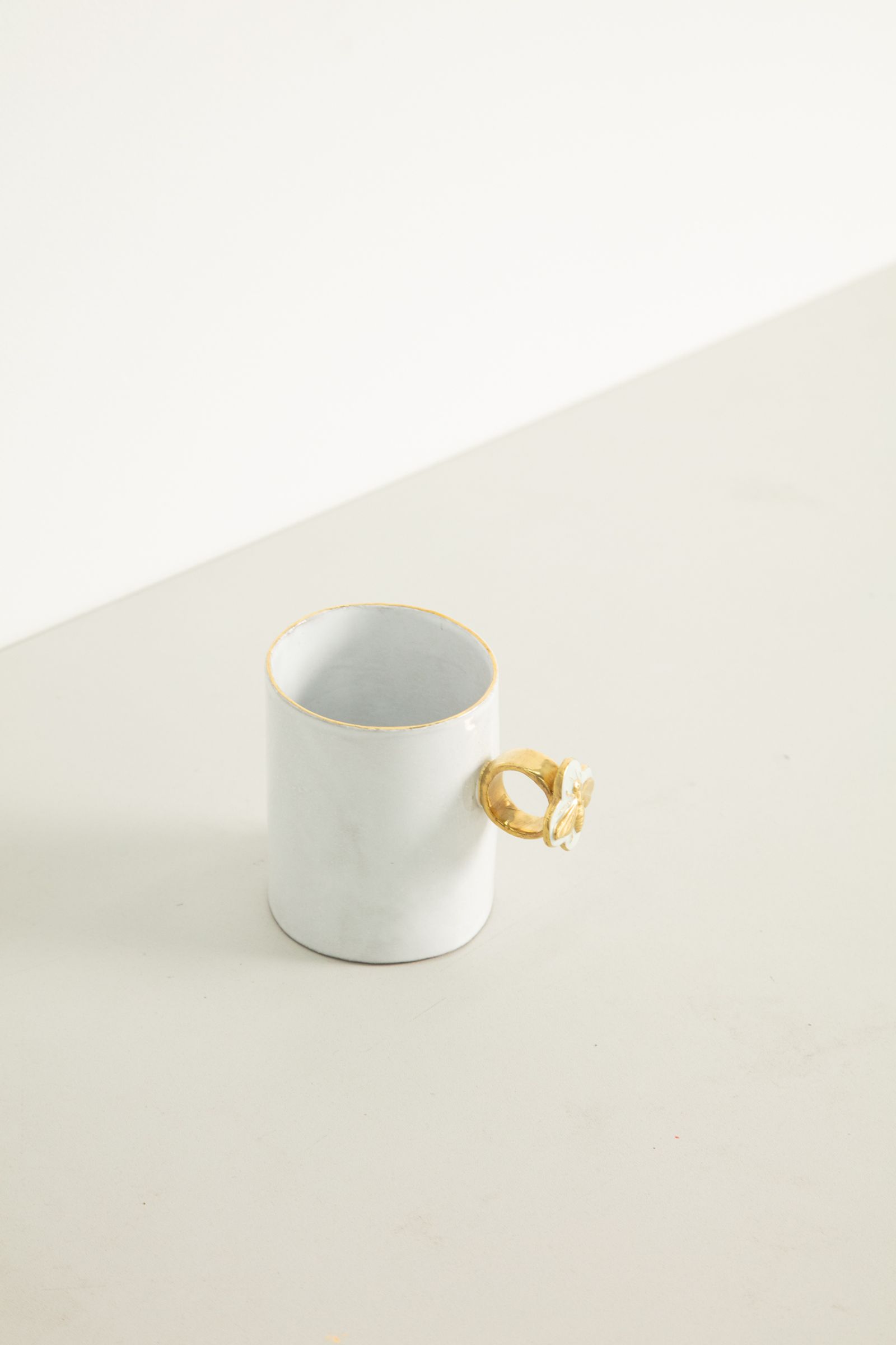 White ceramic cup with bee ornate ring handle. Neutral beige surface.