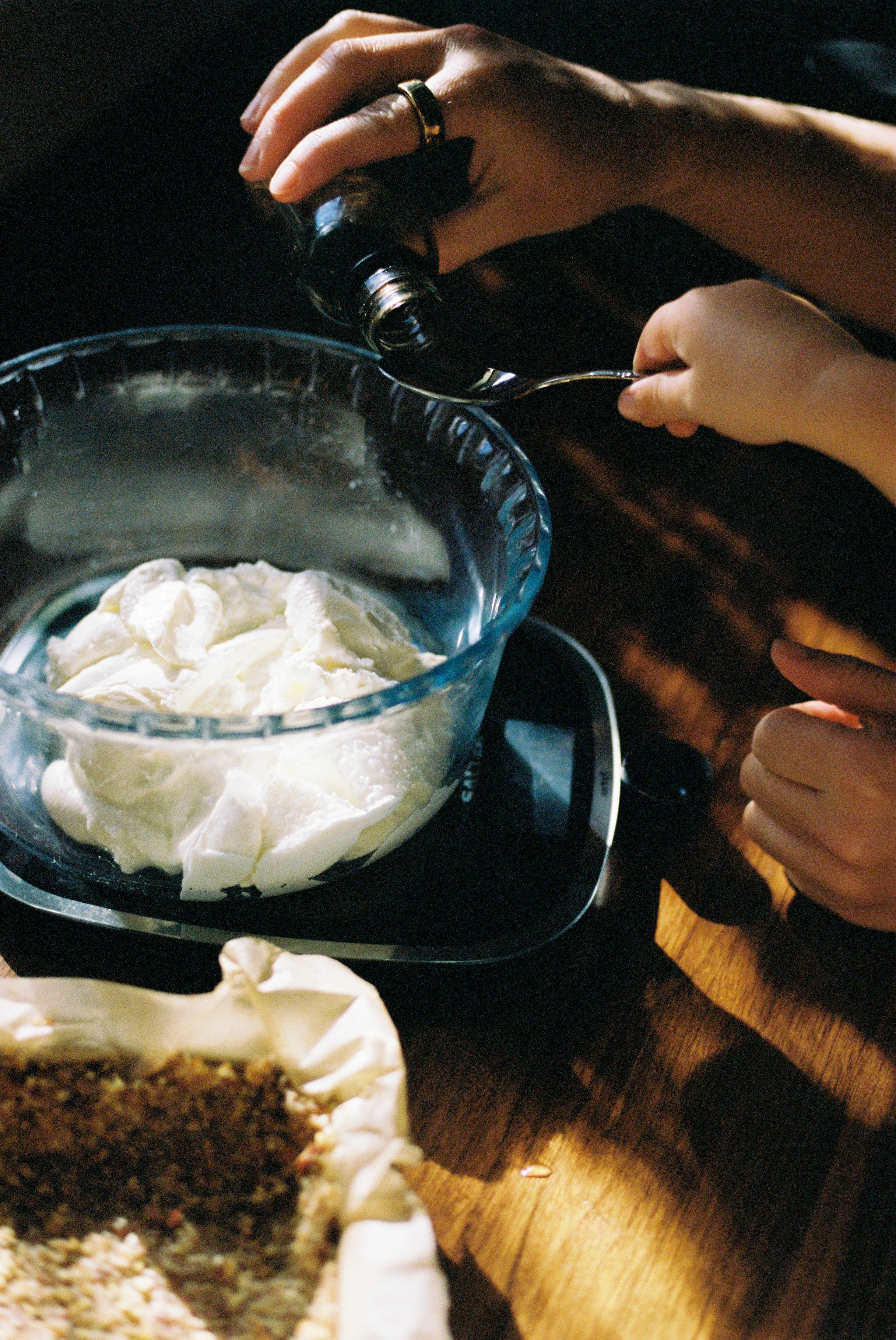 Adult and child hands pouring liquid into cream-filled bowl. Pastry dish in foreground.