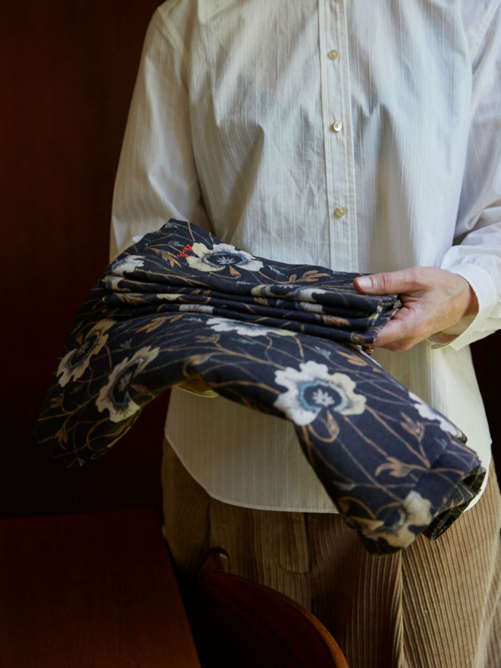 woman holds stack of Berit dark blue linens with floral motif 