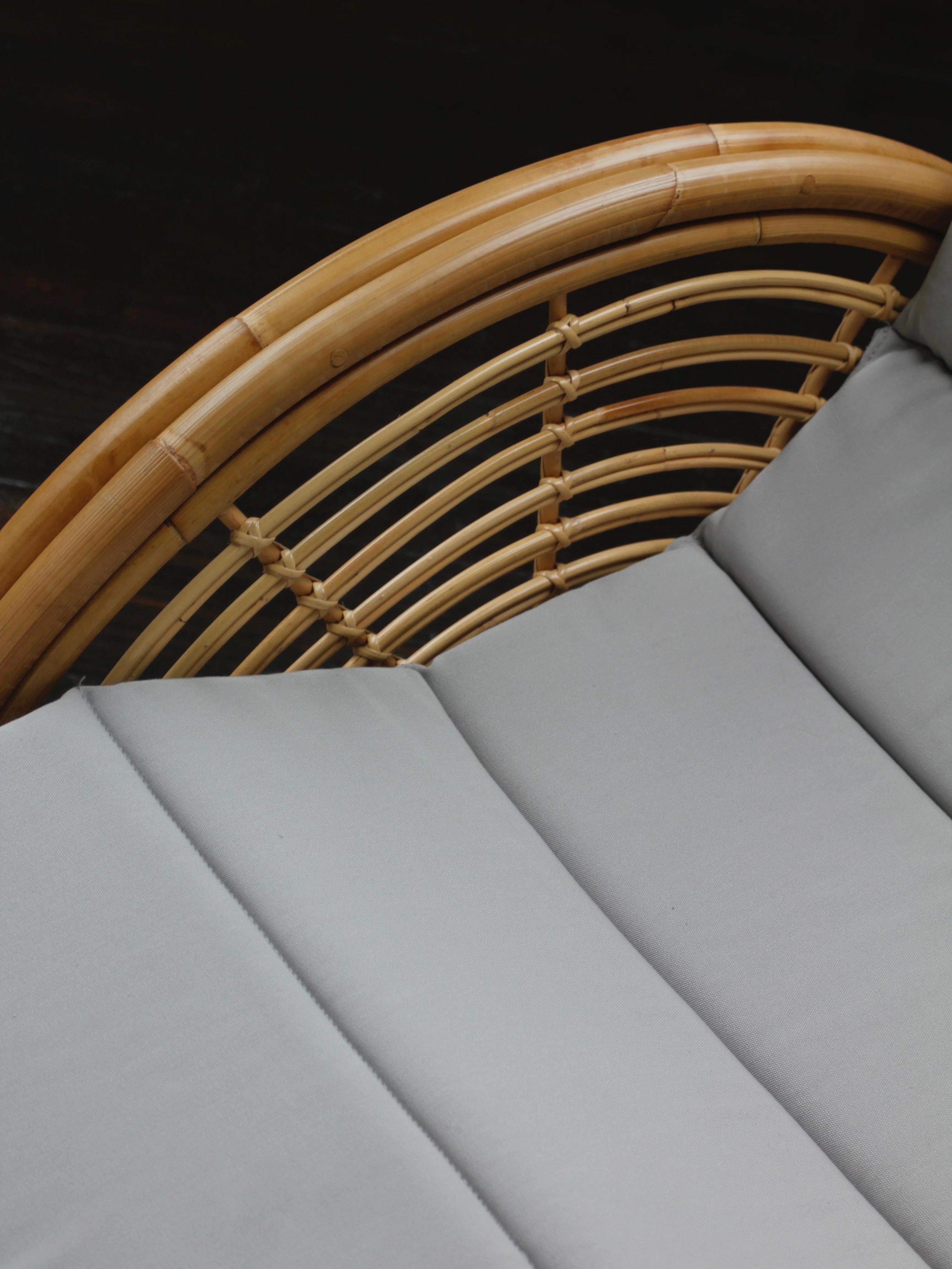 Close-up of a rattan chair headrest with a curved bamboo frame and grey cushioned padding, contrasting with the intricate wicker design.