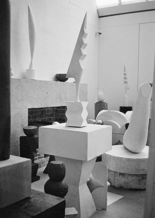 Black and white photo of a gallery displaying abstract and modern sculptures of various shapes and sizes. The sculptures, crafted by homeware artisans, are placed on pedestals, tables, and the floor.